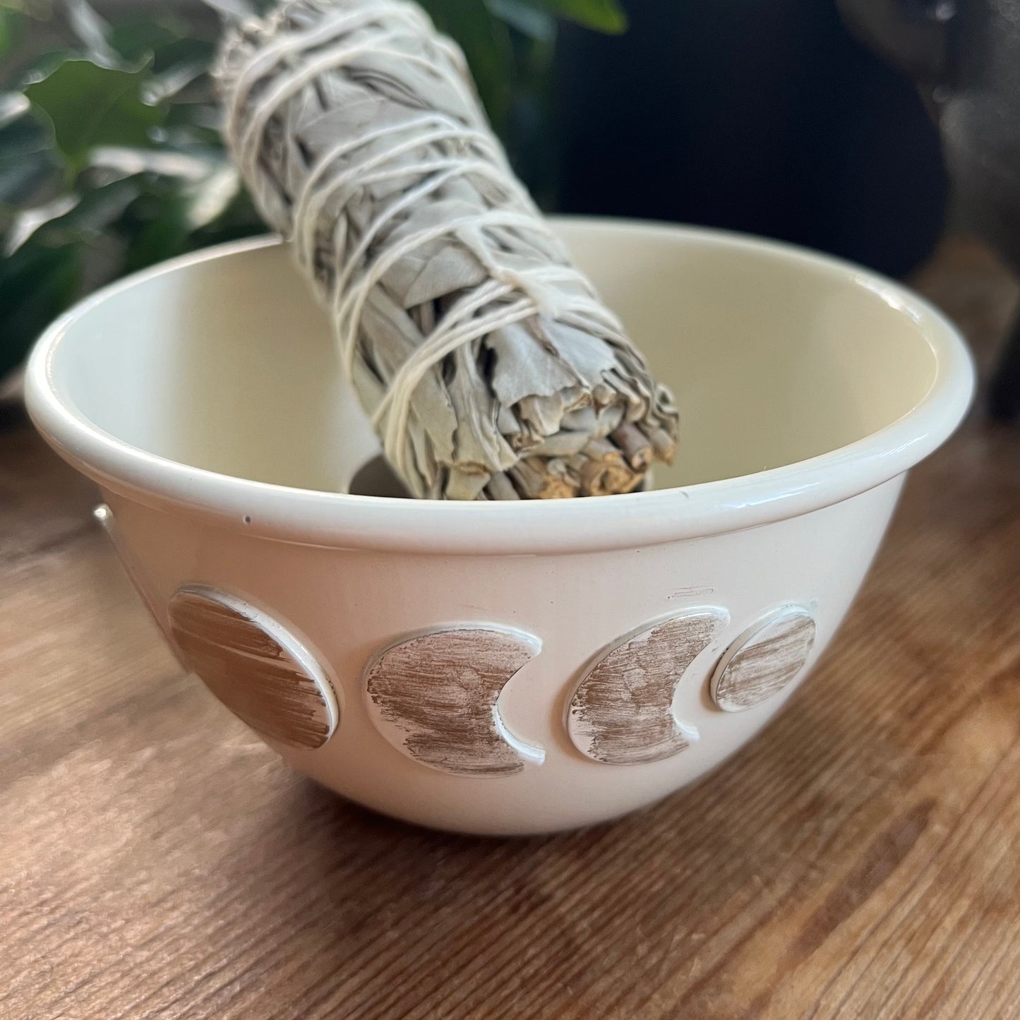 White ceramic moon phase smudge bowl containing a sage bundle on a wooden surface.