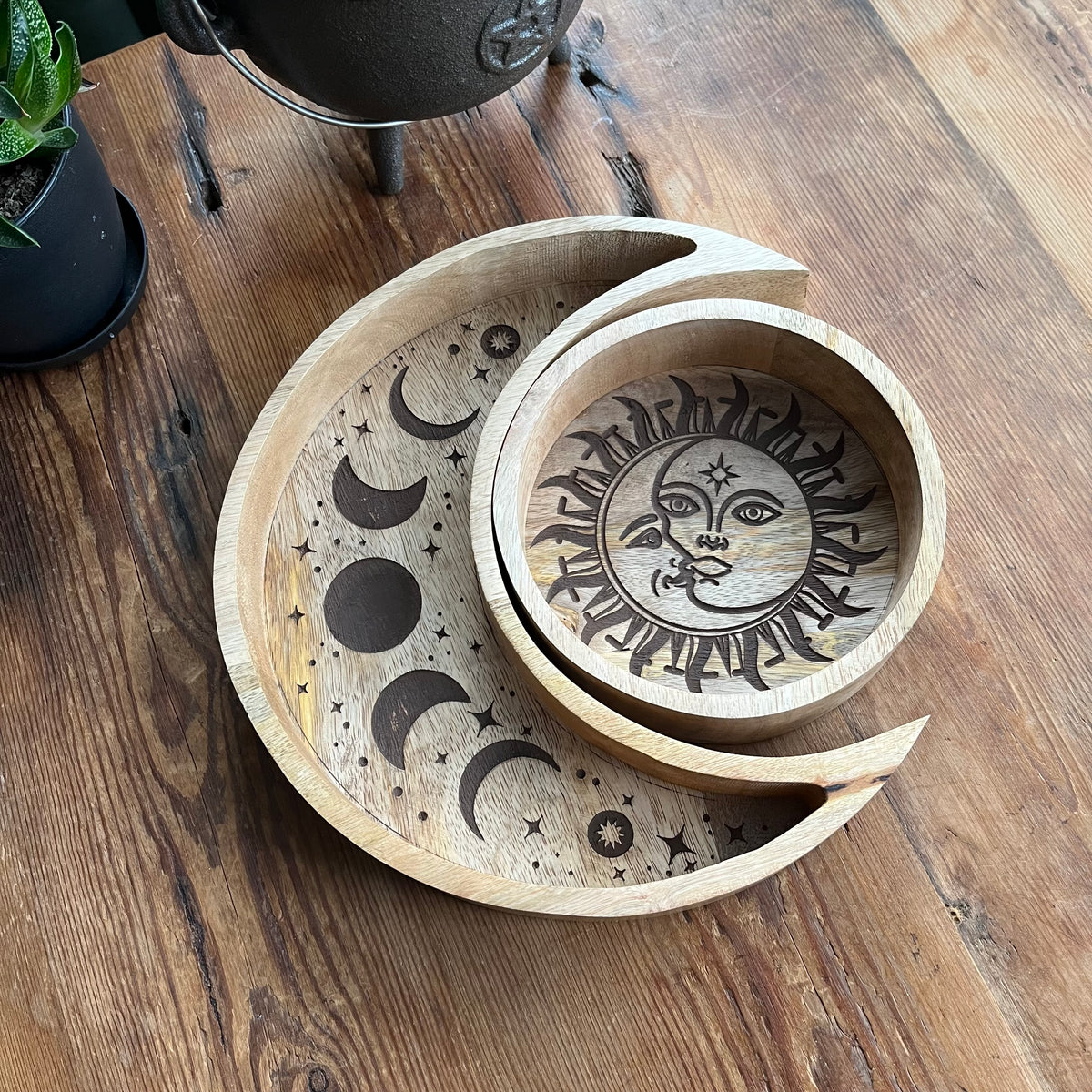 Two nested wooden trays with a celestial moon and sun design, displayed on a rustic wooden table.