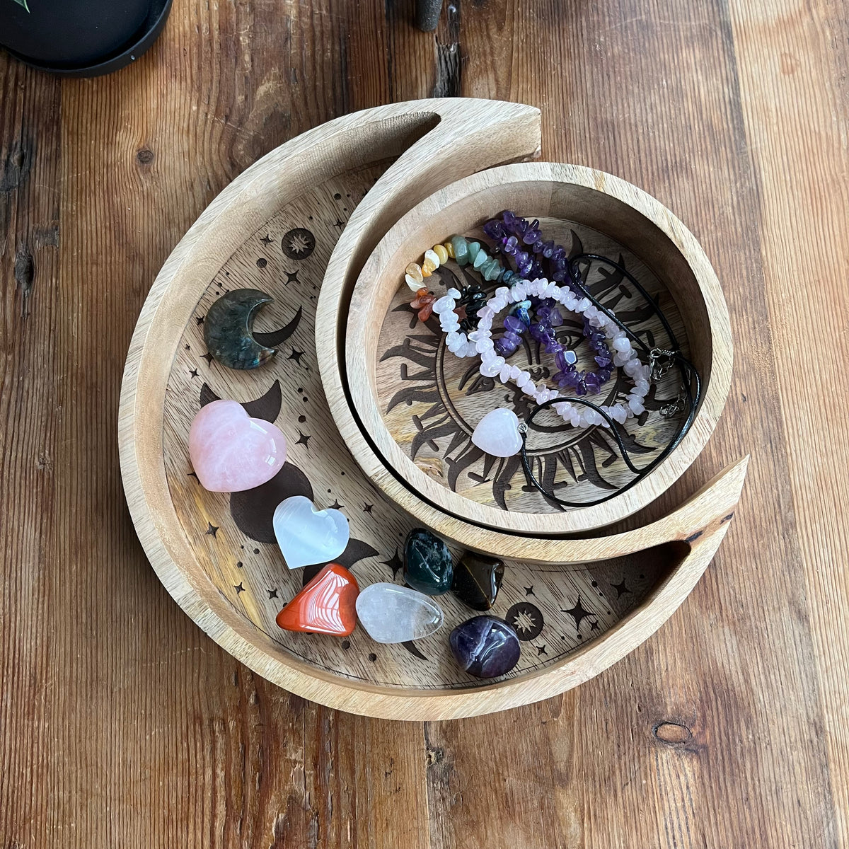 Two nested wooden moon-phase trays filled with crystals and beads, placed on a rustic wooden table.