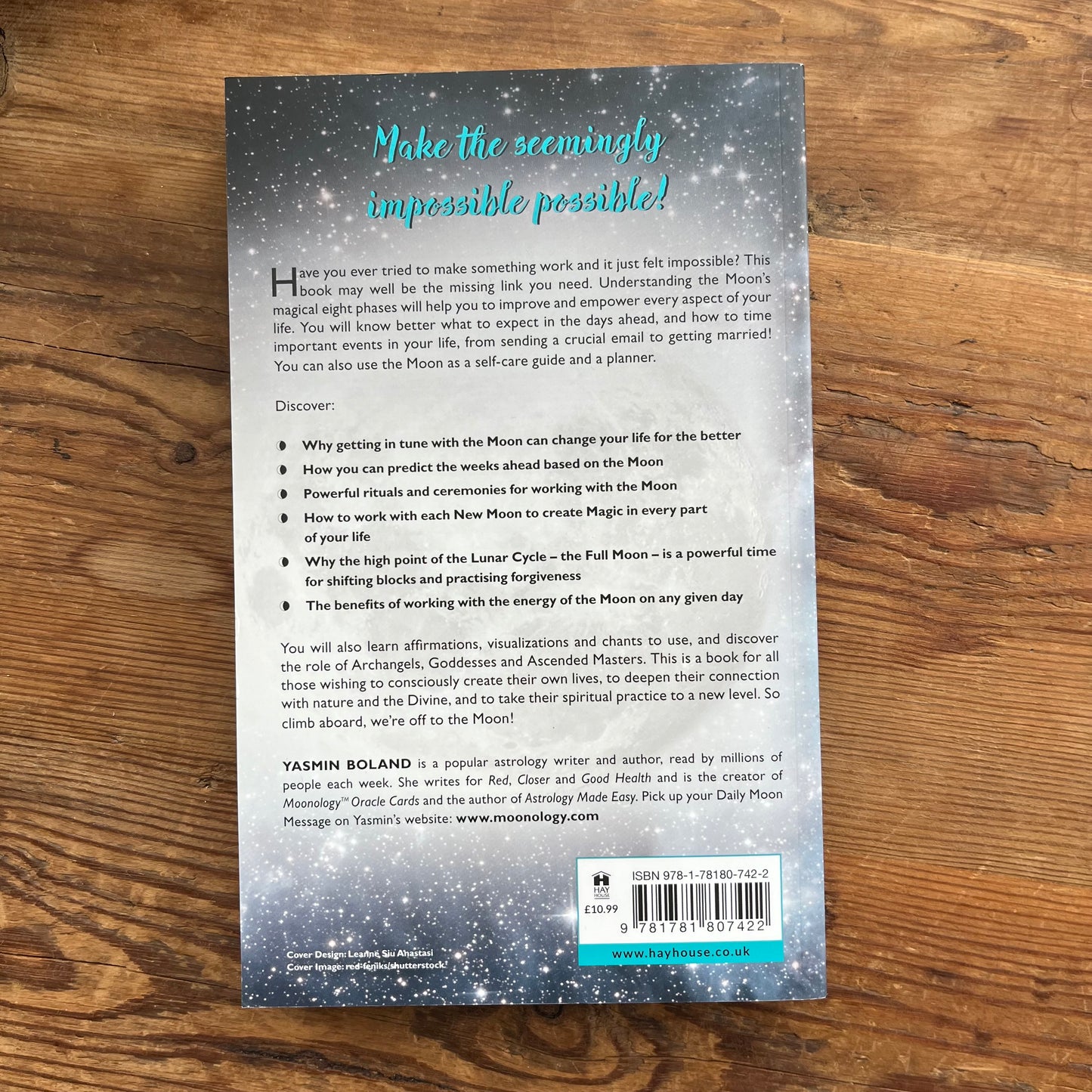 The back cover of the book 'Make the seemingly impossible possible!' by Yasmin Boland, displayed flat on a brown wooden surface. The cover features a dark blue, starry night sky background with glowing moon phases, white text, and a barcode at the bottom.
