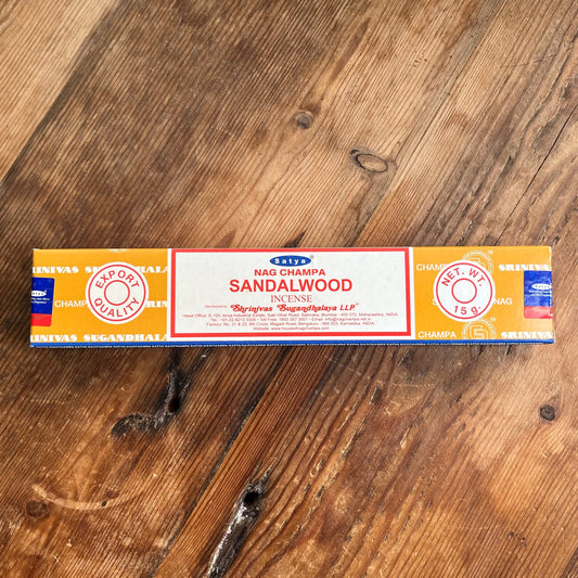 A box of Satya Nag Champa Sandalwood incense, with branding and product information displayed on the packaging, placed on a wooden surface.