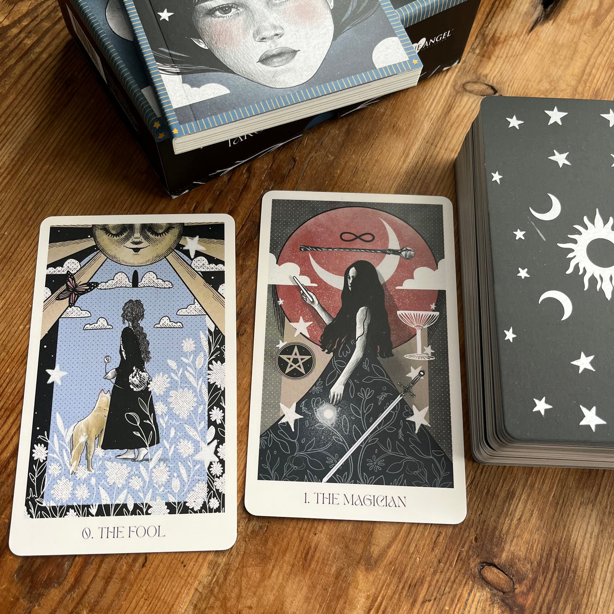 A tarot card deck with illustrated cards displayed on a wooden table. Two cards are laid out face up