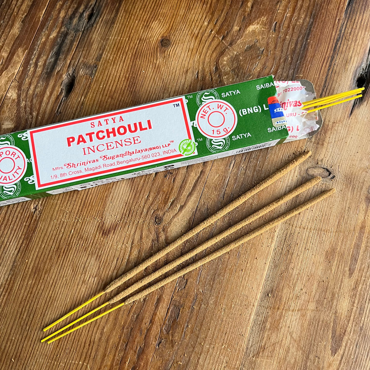 A package of Satya Patchouli Incense along with several loose incense sticks placed on a rustic wooden surface.