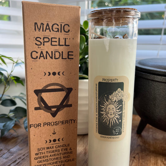 Tall glass spell candle with cork lid. The label on the candle features an image of the sun and the words Prosperity, Tigers Eye And Green Aventurine and Lemon Honeysuckle. The candle itself is White with Tigers Eye and Green Aventurine  gemstones embedded within it. Alongside the glass Magic spell candle is it's brown cardboard box which has the words magic spell candle for Prosperity, soy wax candle with Tigers Eye and Green Aventurine  gemstones and Lemon Honeysuckle fragrance.