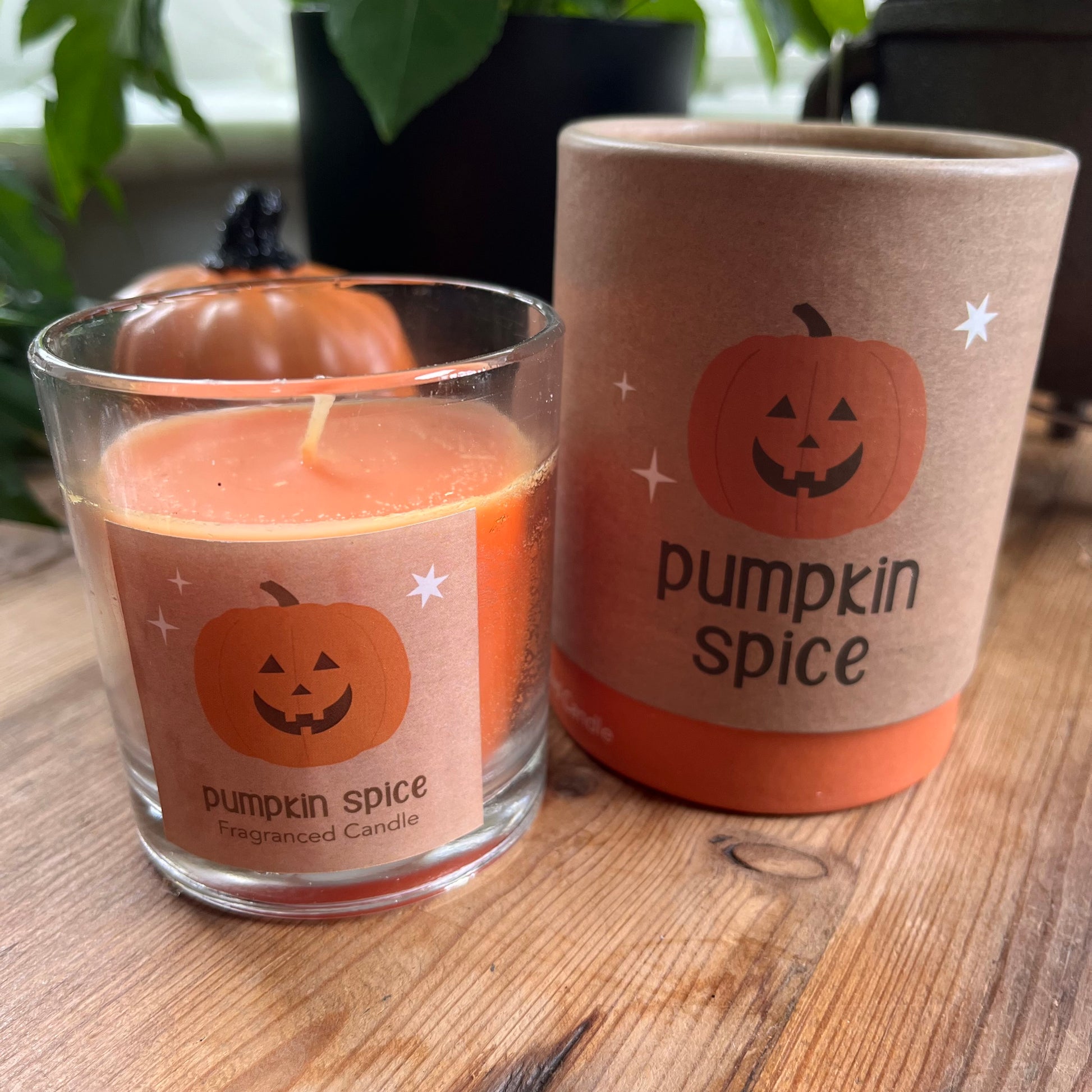 Pumpkin spice candle and mug on a wooden surface with pumpkins in the background