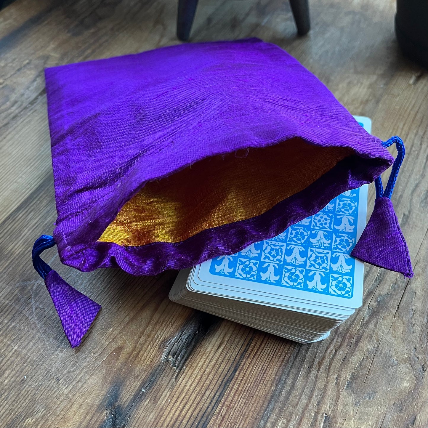 Purple drawstring bag with yellow interior next to a deck of cards on a wooden surface