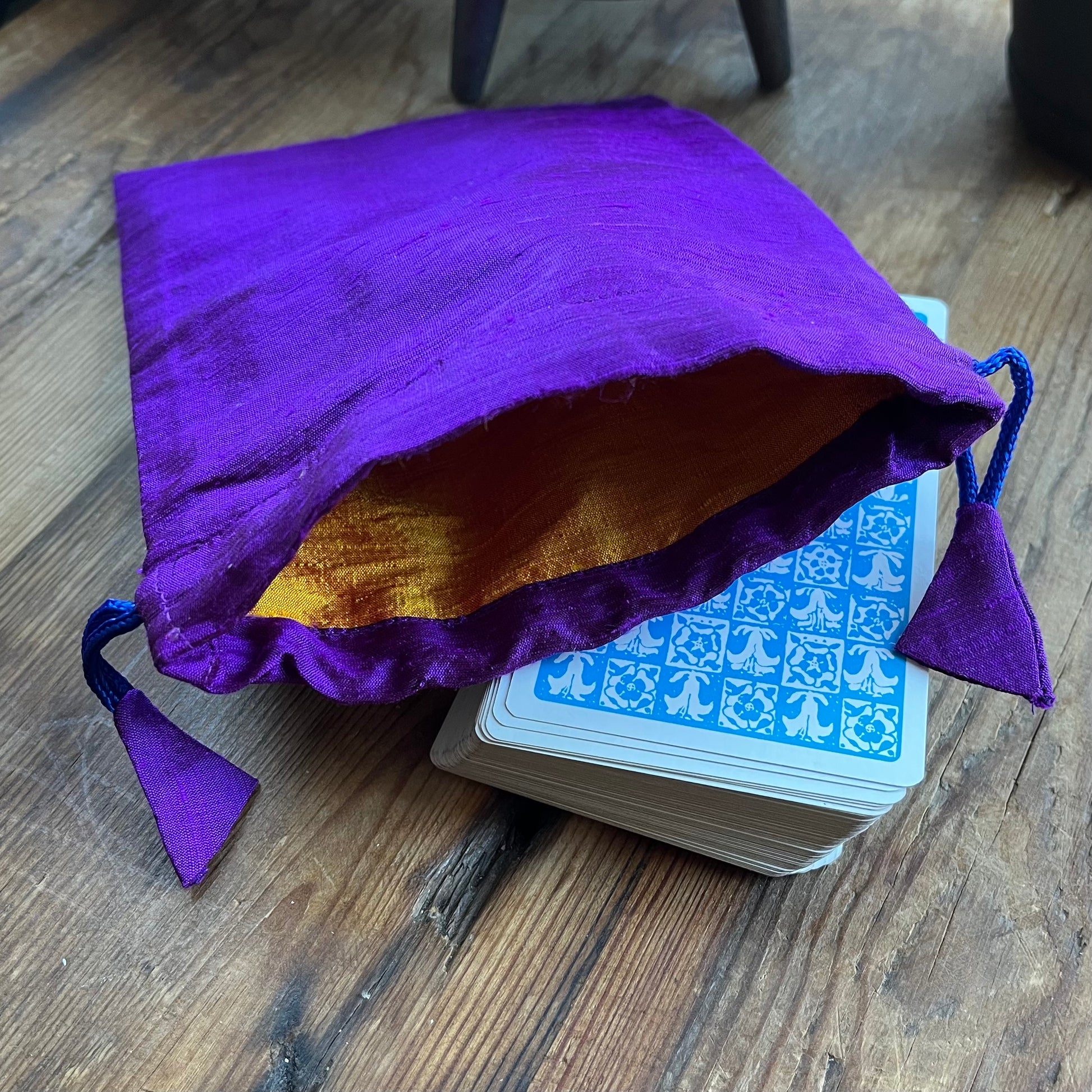 Purple drawstring bag with yellow interior next to a deck of cards on a wooden surface