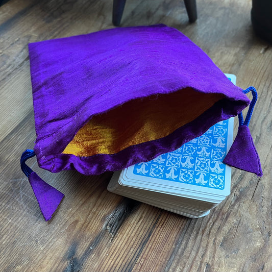 Purple drawstring bag with yellow interior next to a deck of cards on a wooden surface