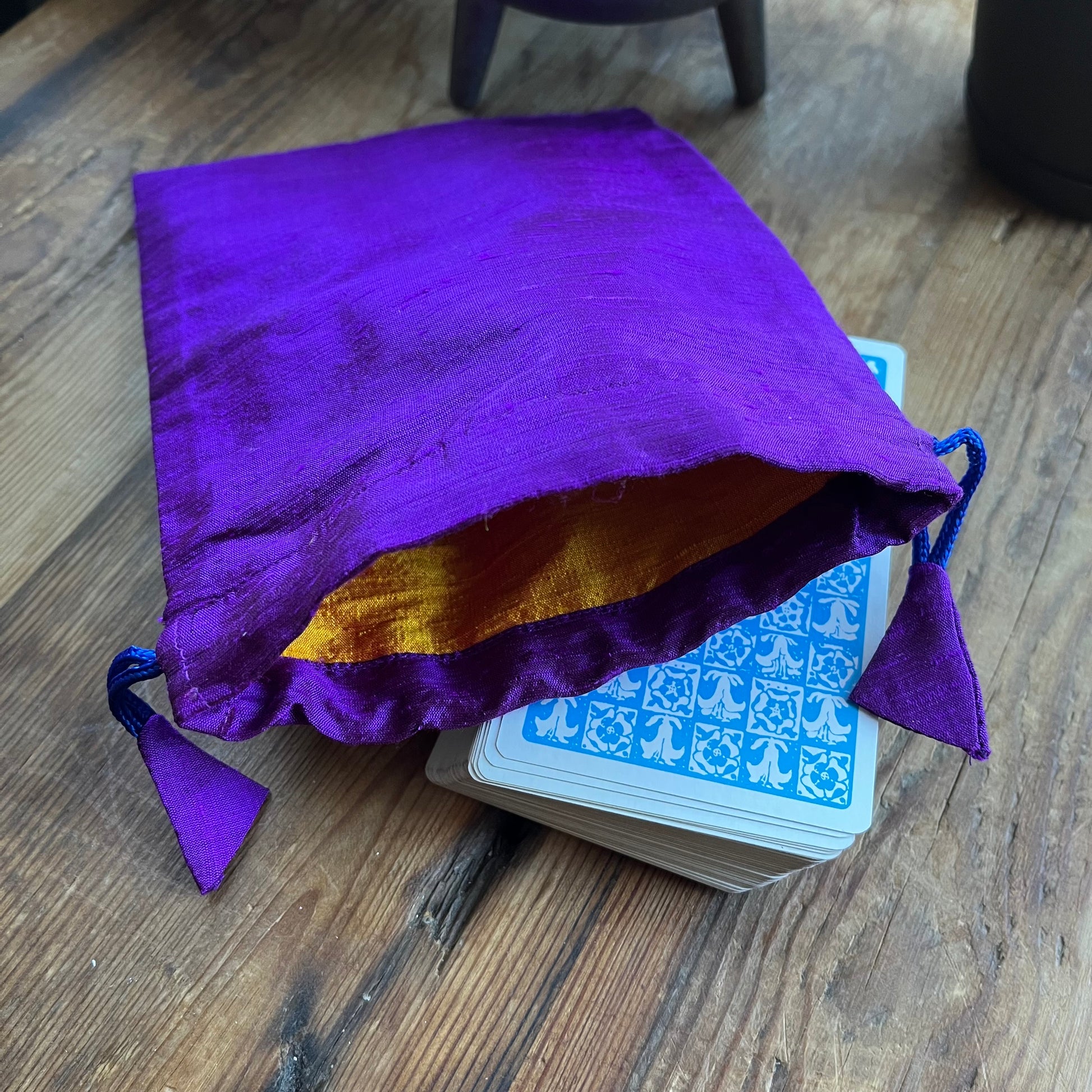 Purple drawstring bag with gold interior containing a deck of cards on a wooden surface