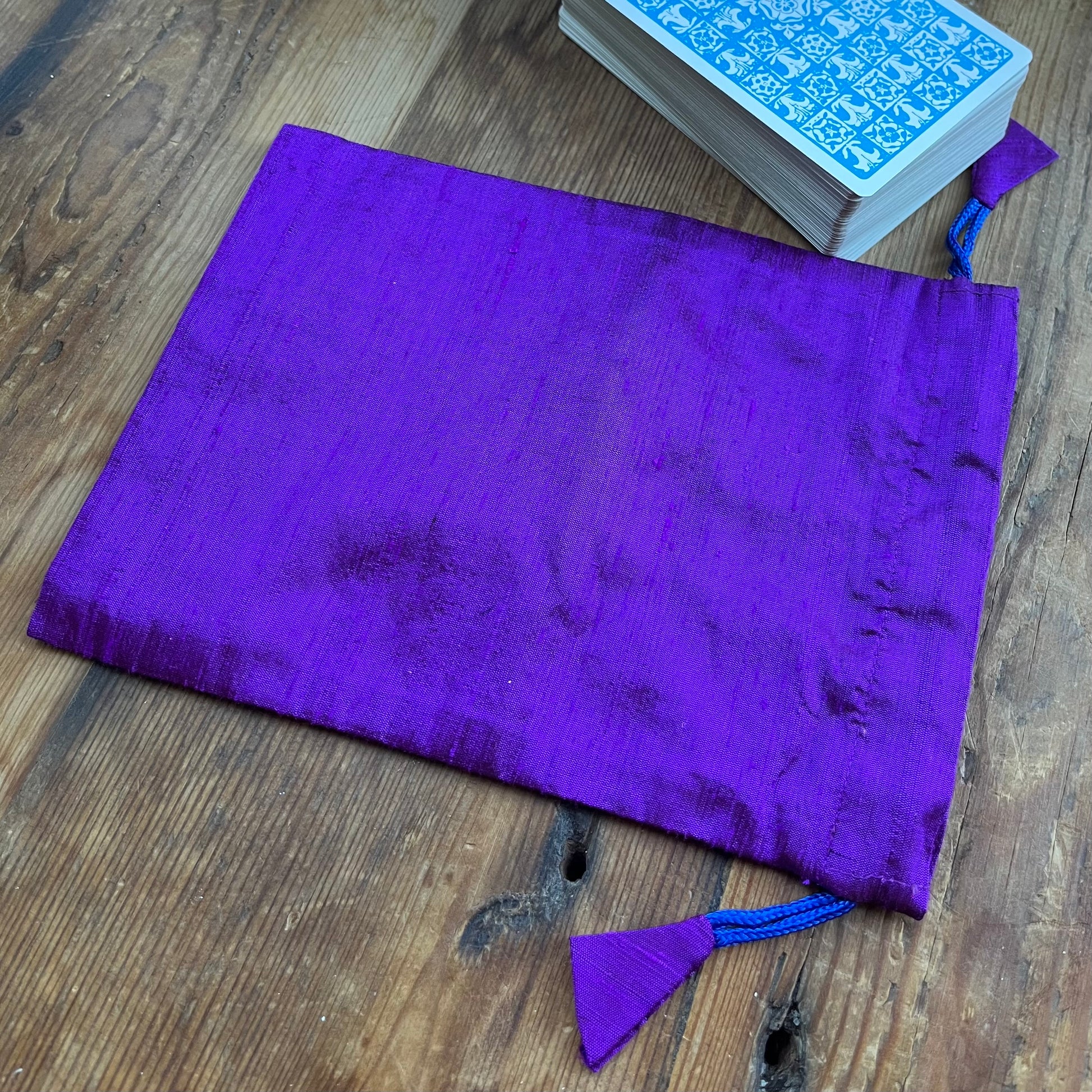 Purple drawstring bag on a wooden surface with blue patterned cards.