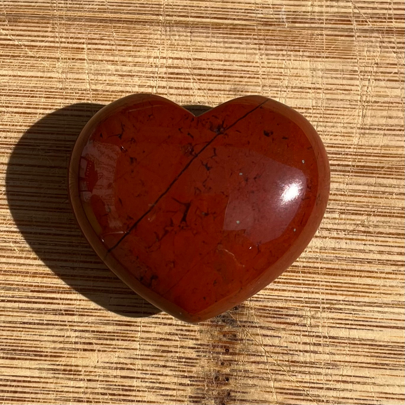 A heart-shaped polished red stone with dark veining, resting on a light brown textured bamboo mat.