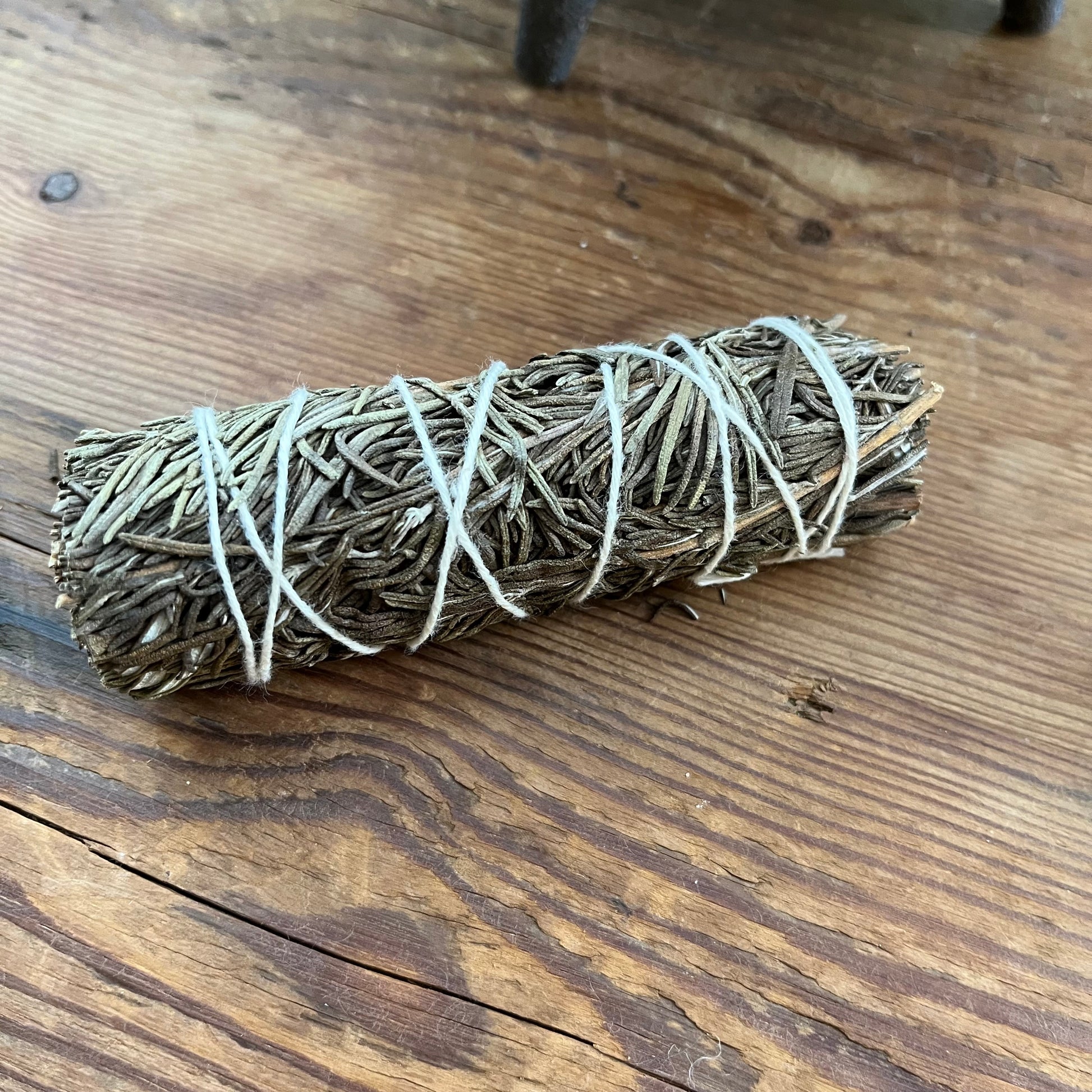 A natural dried herb smudge bundle wrapped in white string, resting on a rustic wooden tabletop.