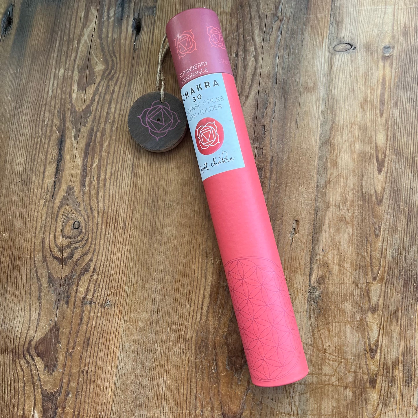 Red cardboard tube holding strawberry scented incense for the Root Chakra with a wooden incense holder with the symbol for the root chakra printed onto it. 