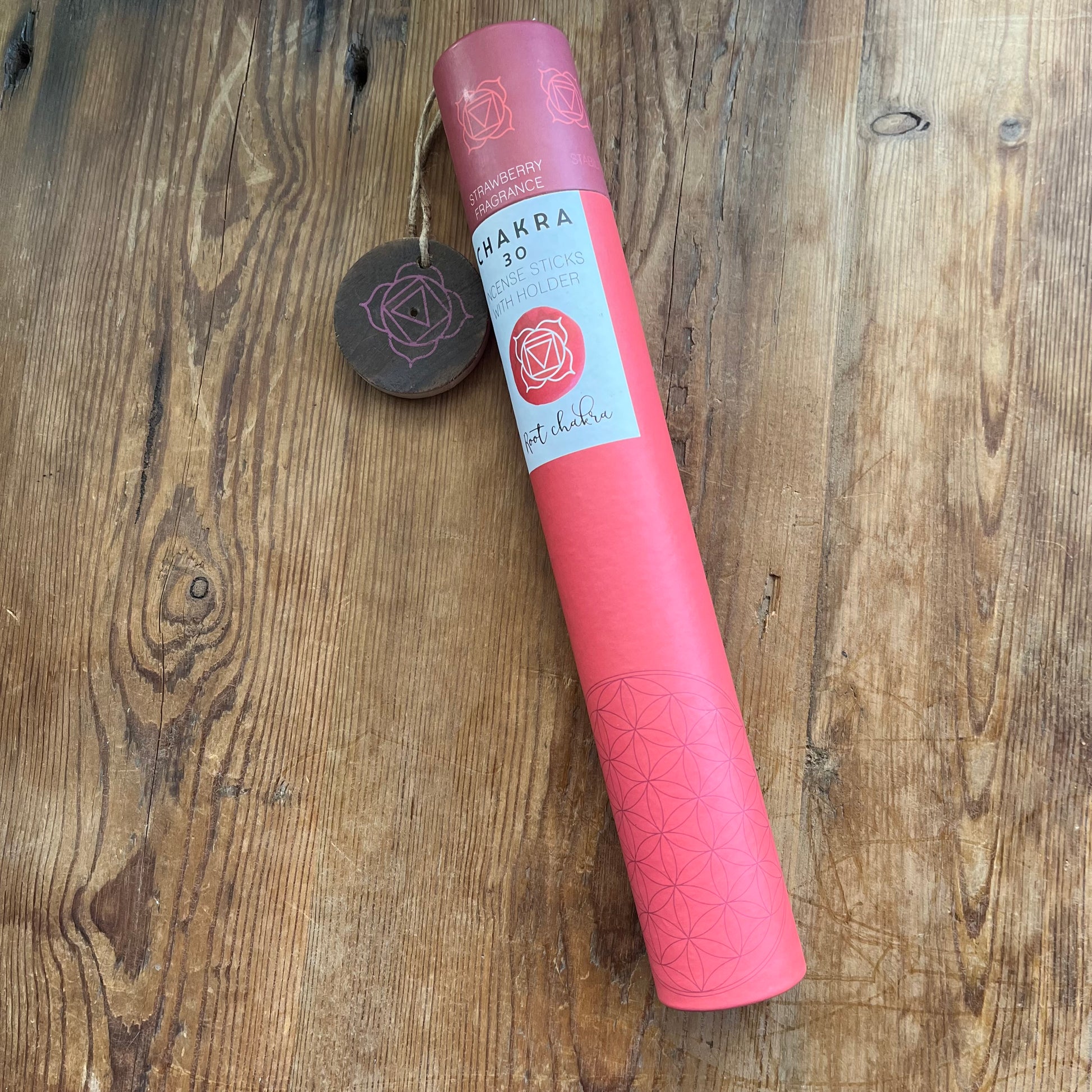 Red cardboard tube holding strawberry scented incense for the Root Chakra with a wooden incense holder with the symbol for the root chakra printed onto it. 