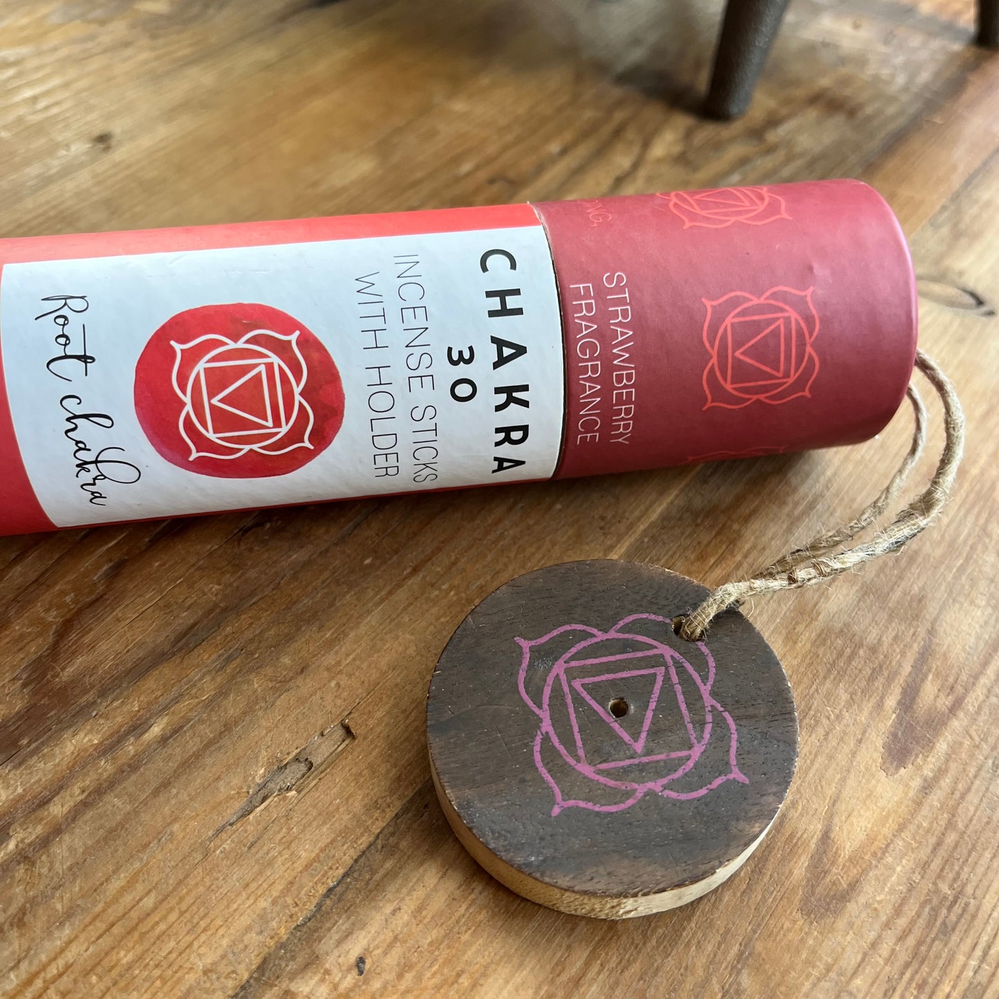 Red cardboard tube holding strawberry scented incense for the Root Chakra with a wooden incense holder with the symbol for the root chakra printed onto it. 