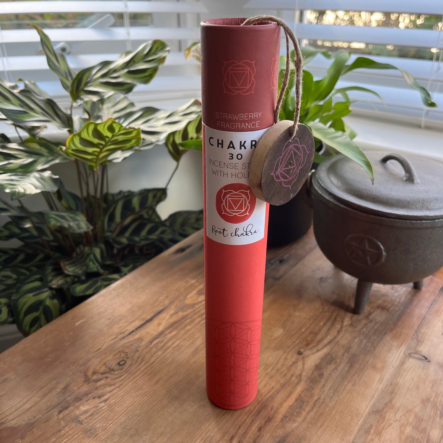 Red cardboard tube holding strawberry scented incense for the Root Chakra with a wooden incense holder with the symbol for the root chakra printed onto it. 