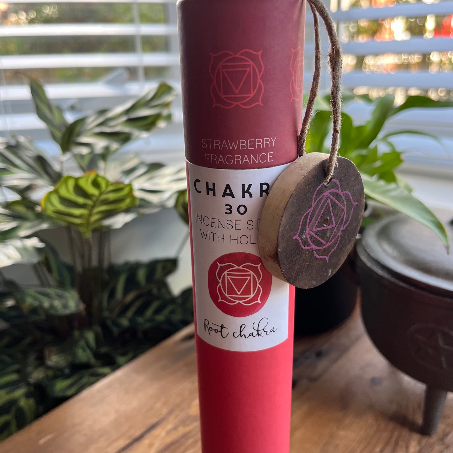 Red cardboard tube holding strawberry scented incense for the Root Chakra with a wooden incense holder with the symbol for the root chakra printed onto it. 