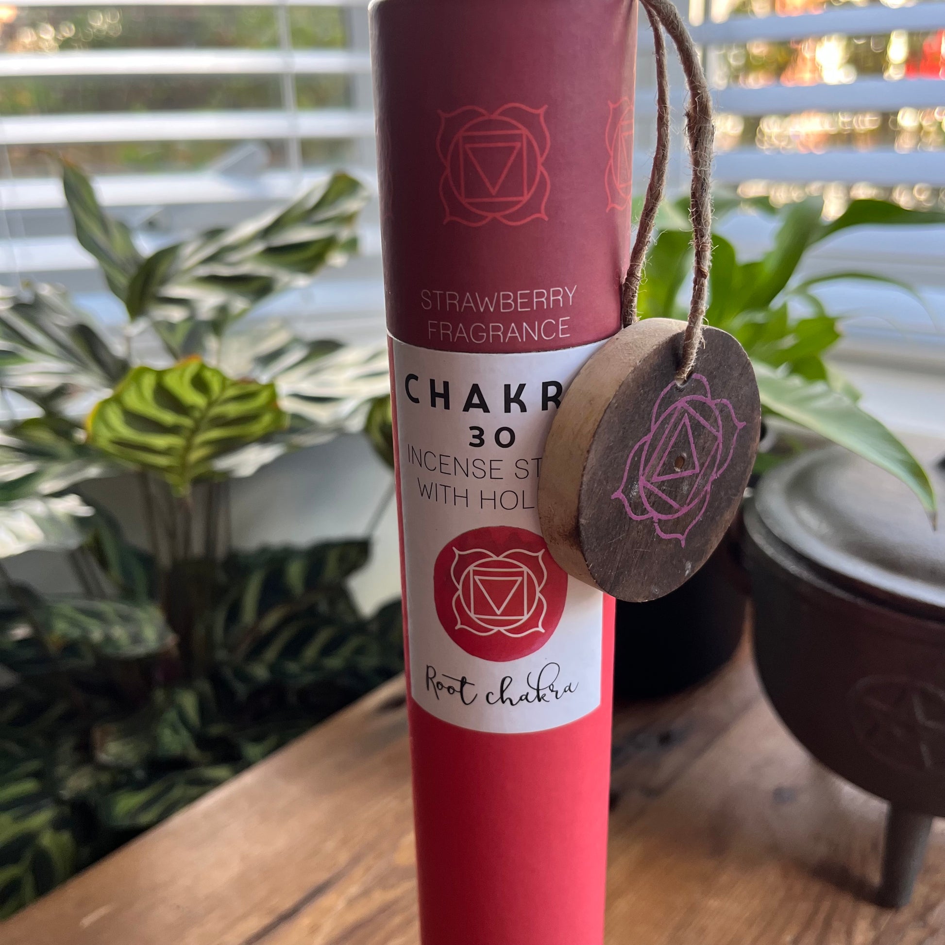 Red cardboard tube holding strawberry scented incense for the Root Chakra with a wooden incense holder with the symbol for the root chakra printed onto it. 
