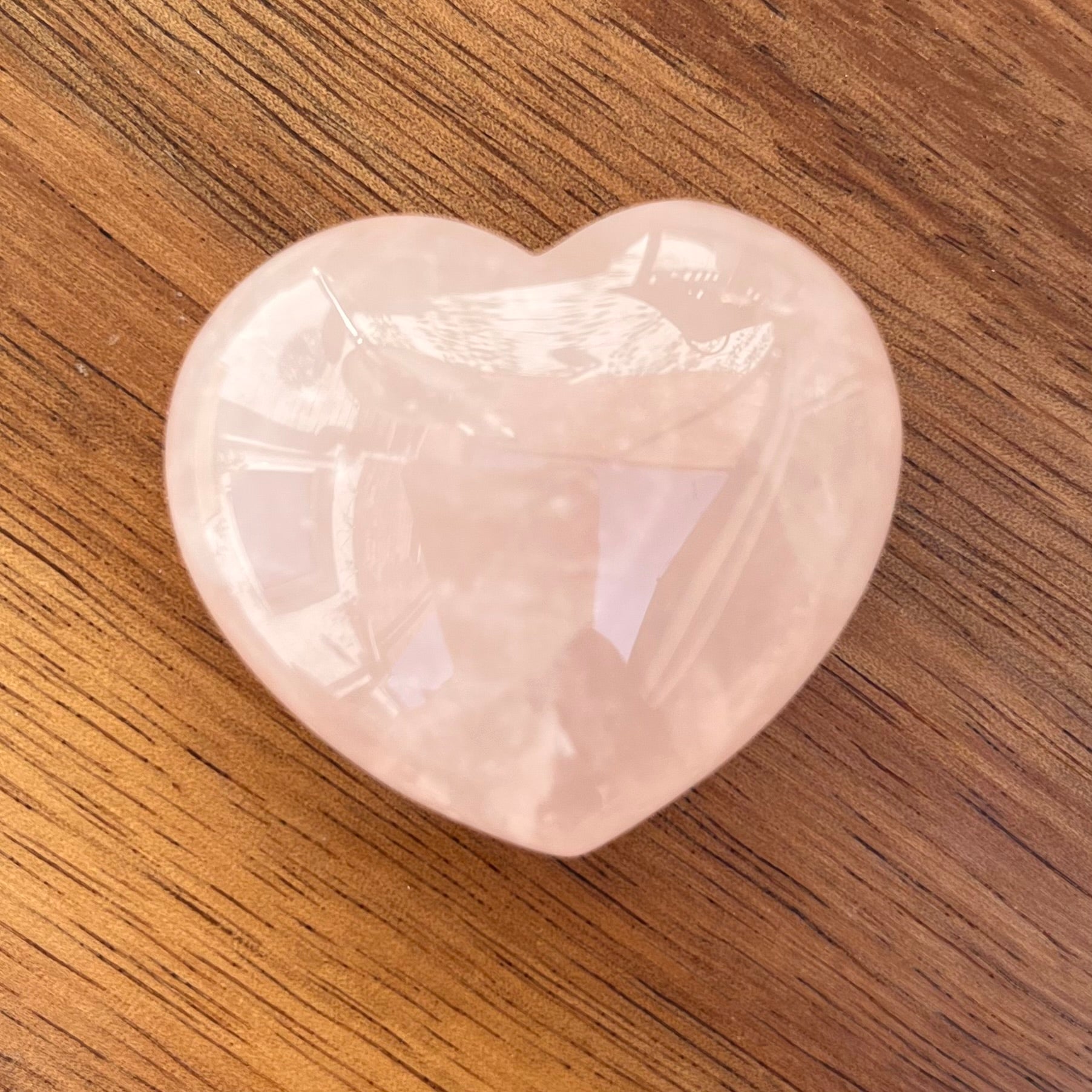 A polished heart-shaped rose quartz crystal resting on a brown wooden surface.