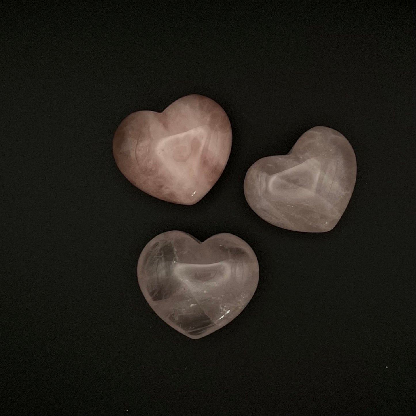Three heart-shaped rose quartz crystals arranged on a solid black background.