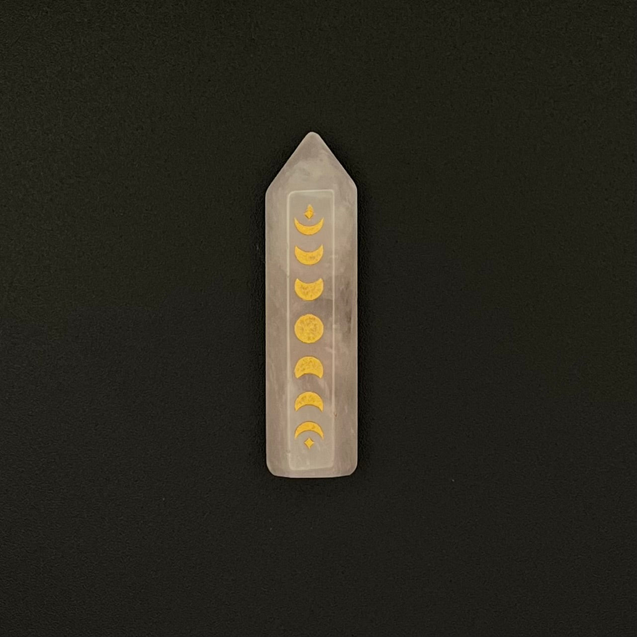 A Rose Quartz crystal point wand featuring a vertical series of gold moon phases, set against a solid black background.