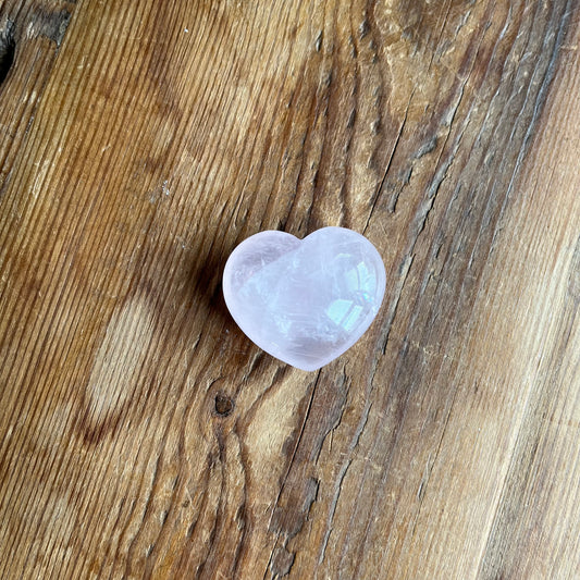 A polished heart-shaped rose quartz crystal resting on a rustic, textured wooden surface.