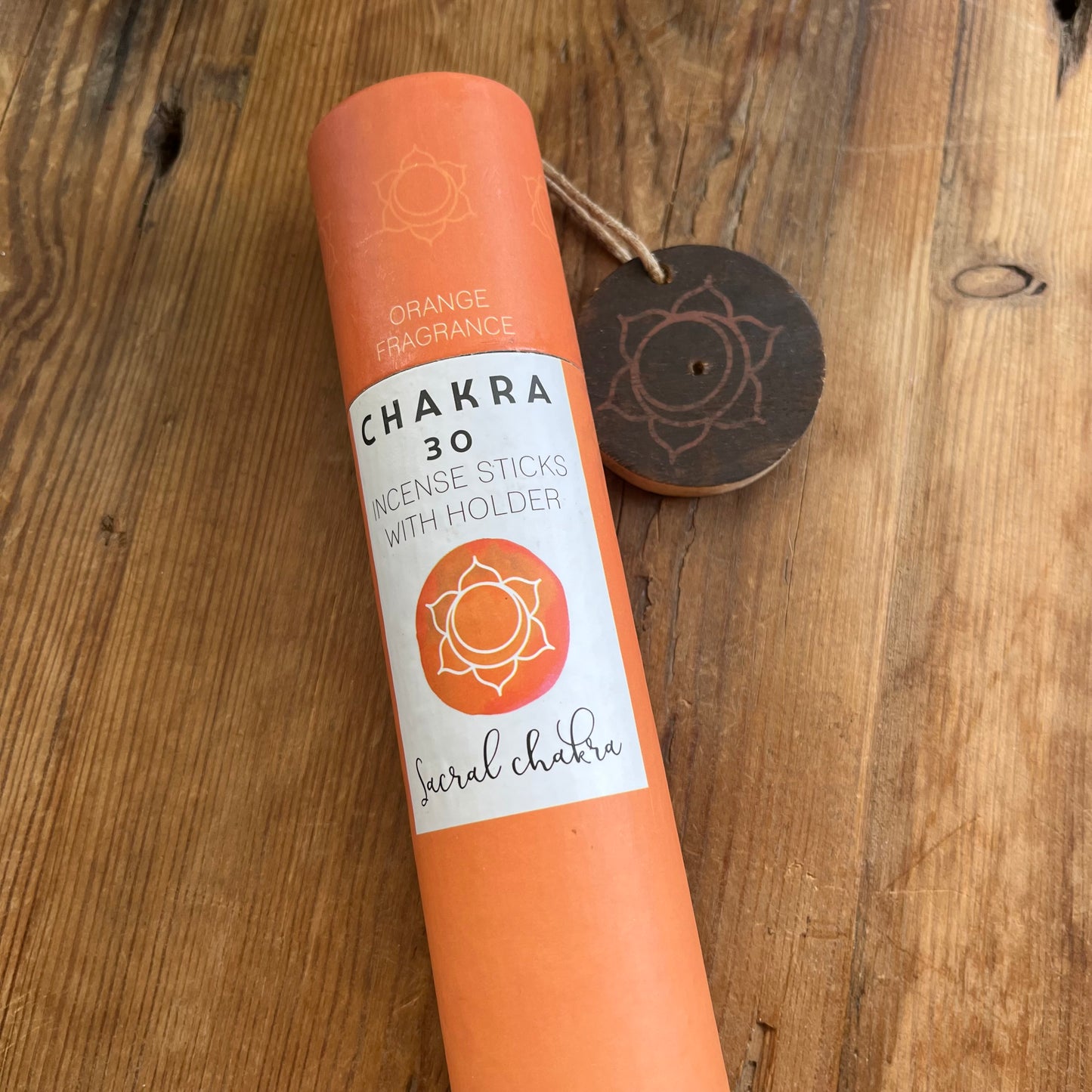 Orange cardboard tube containing 30 sticks of orange scented incense for the Sacral Chakra with a wooden incense holder printed with the Sacral Chakra symbol 