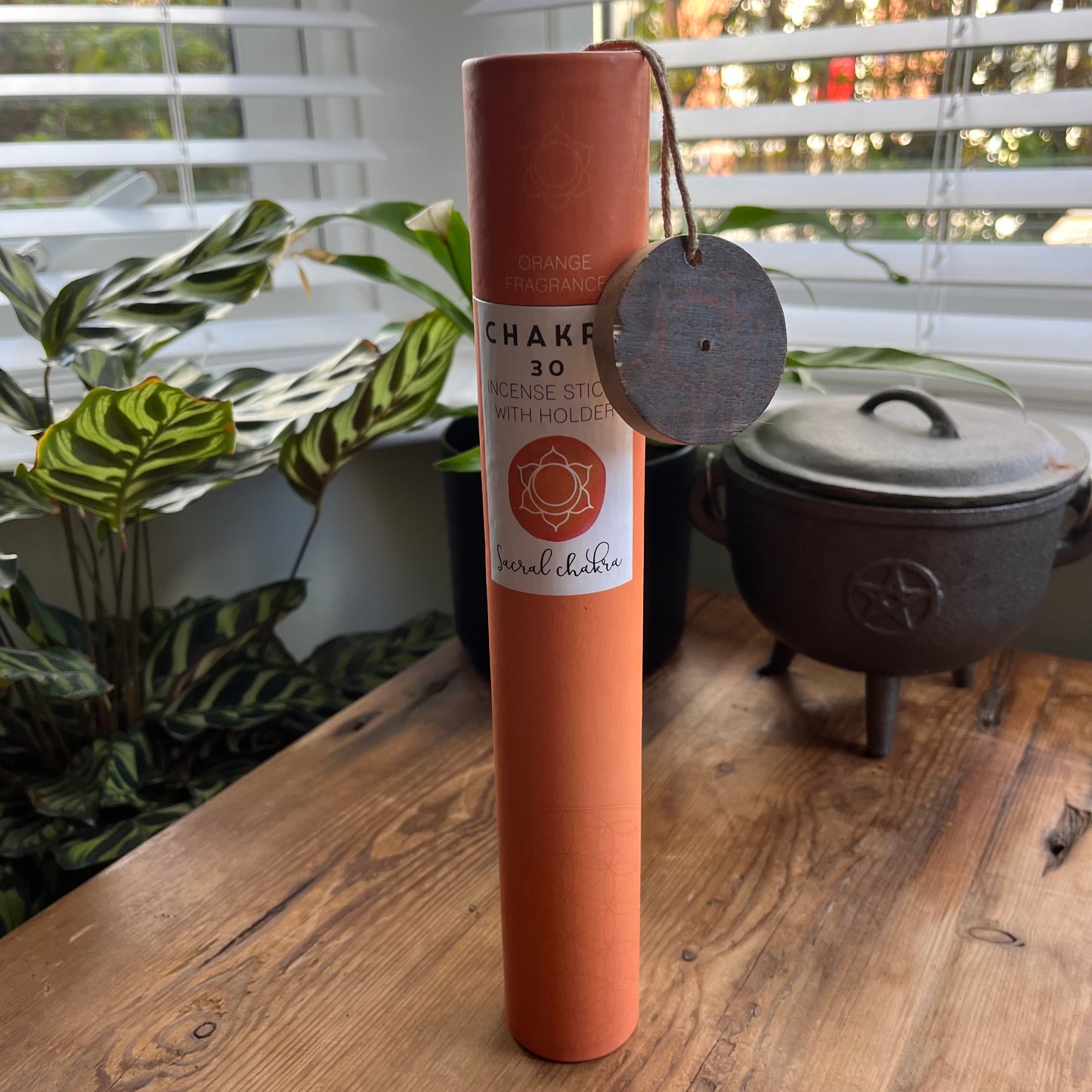 Orange cardboard tube containing 30 sticks of orange scented incense for the Sacral Chakra with a wooden incense holder printed with the Sacral Chakra symbol 