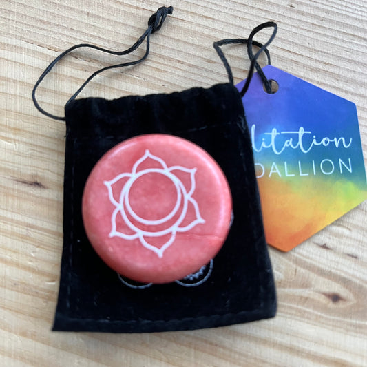  colourful circular flat meditation stone engraved with the Sacral Chakra symbol, alongside it's black velvet pouch 