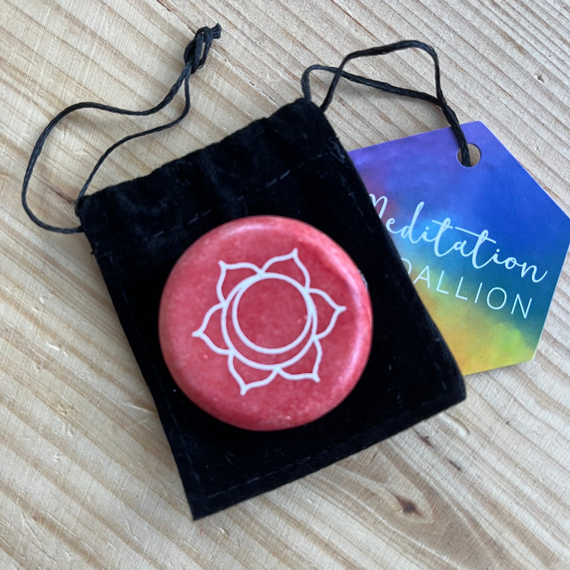  colourful circular flat meditation stone engraved with the Sacral Chakra symbol, alongside it's black velvet pouch 