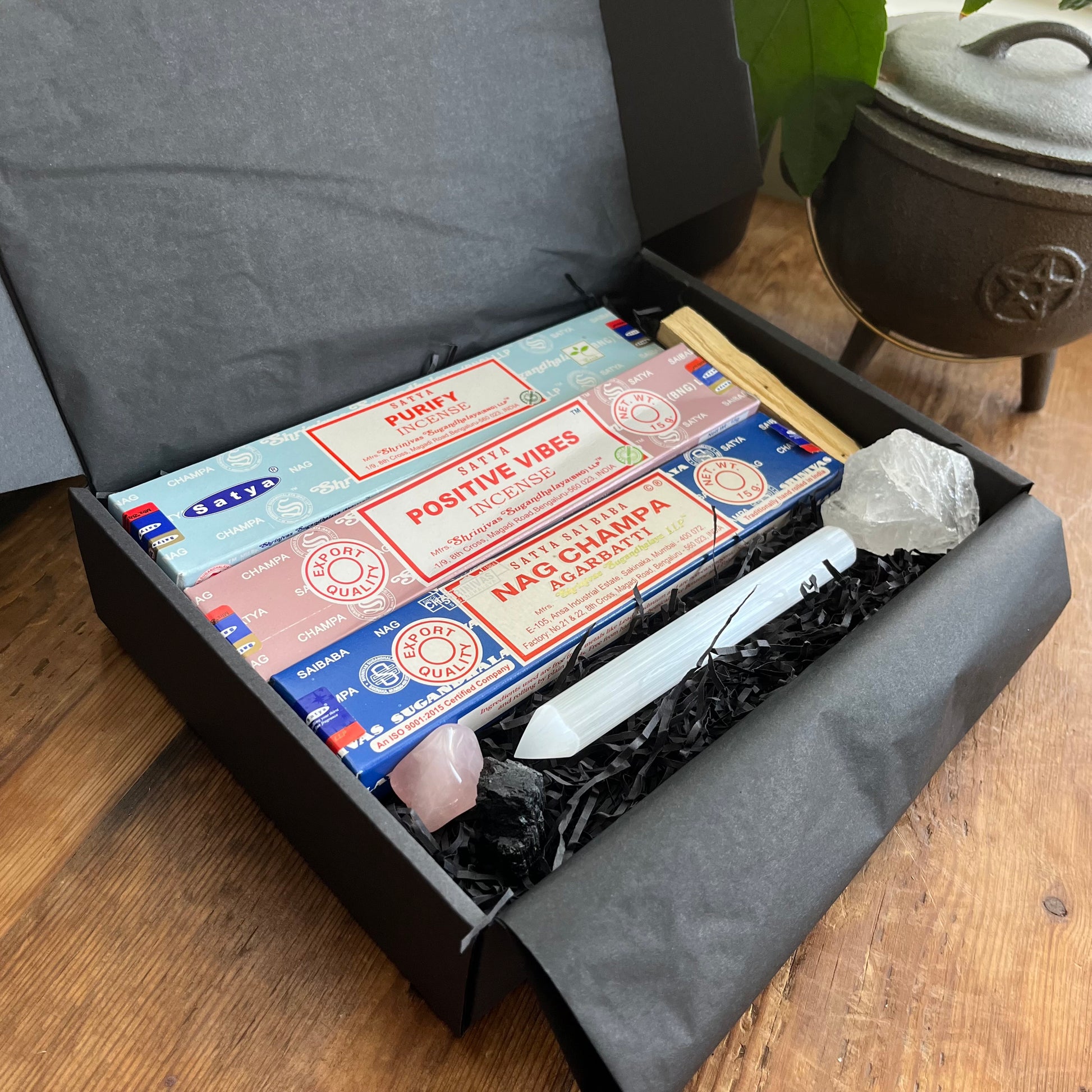 Incense sticks in a black box with a crystal and other items on a wooden surface.