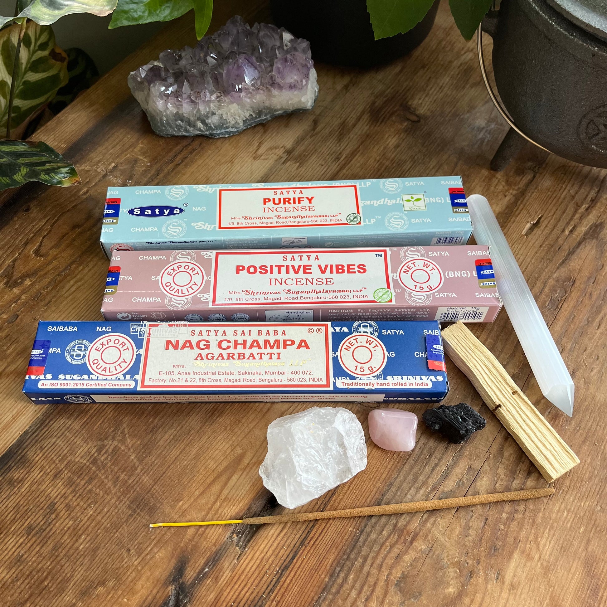Three Satya incense stick boxes on a wooden surface with crystals and sticks.