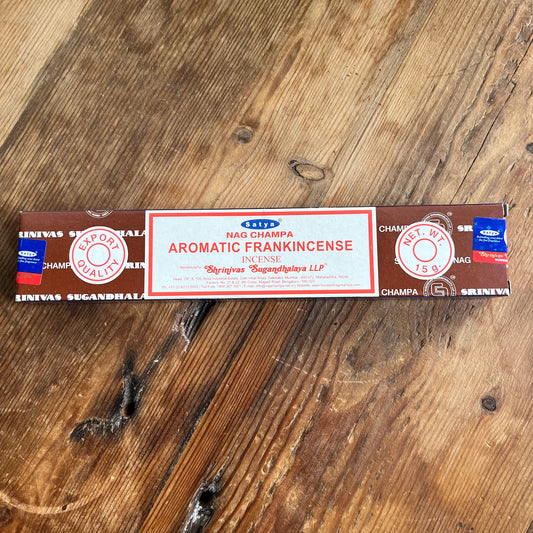 A package of Satya Nag Champa Aromatic Frankincense incense is displayed on a wooden surface.