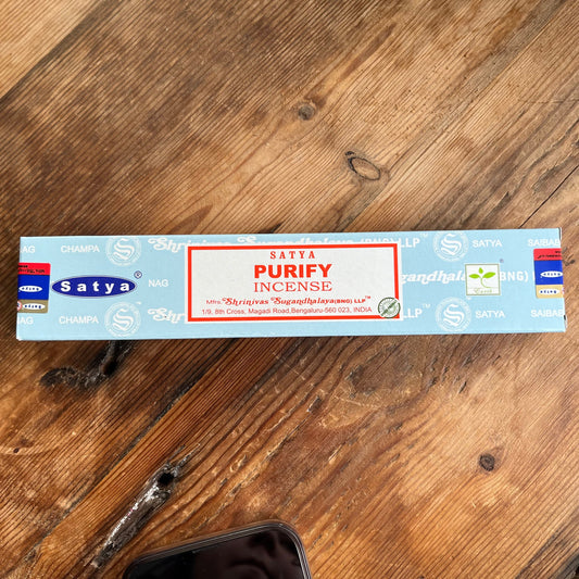 A box of Satya Purify incense placed on a wooden surface, with the brand name and product description visible.