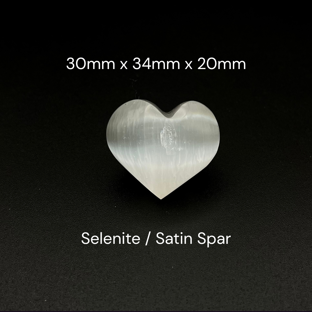 A heart-shaped selenite stone on a black background, with white text overlay showing dimensions '30mm x 34mm x 20mm' and the material name 'Selenite / Satin Spar'.