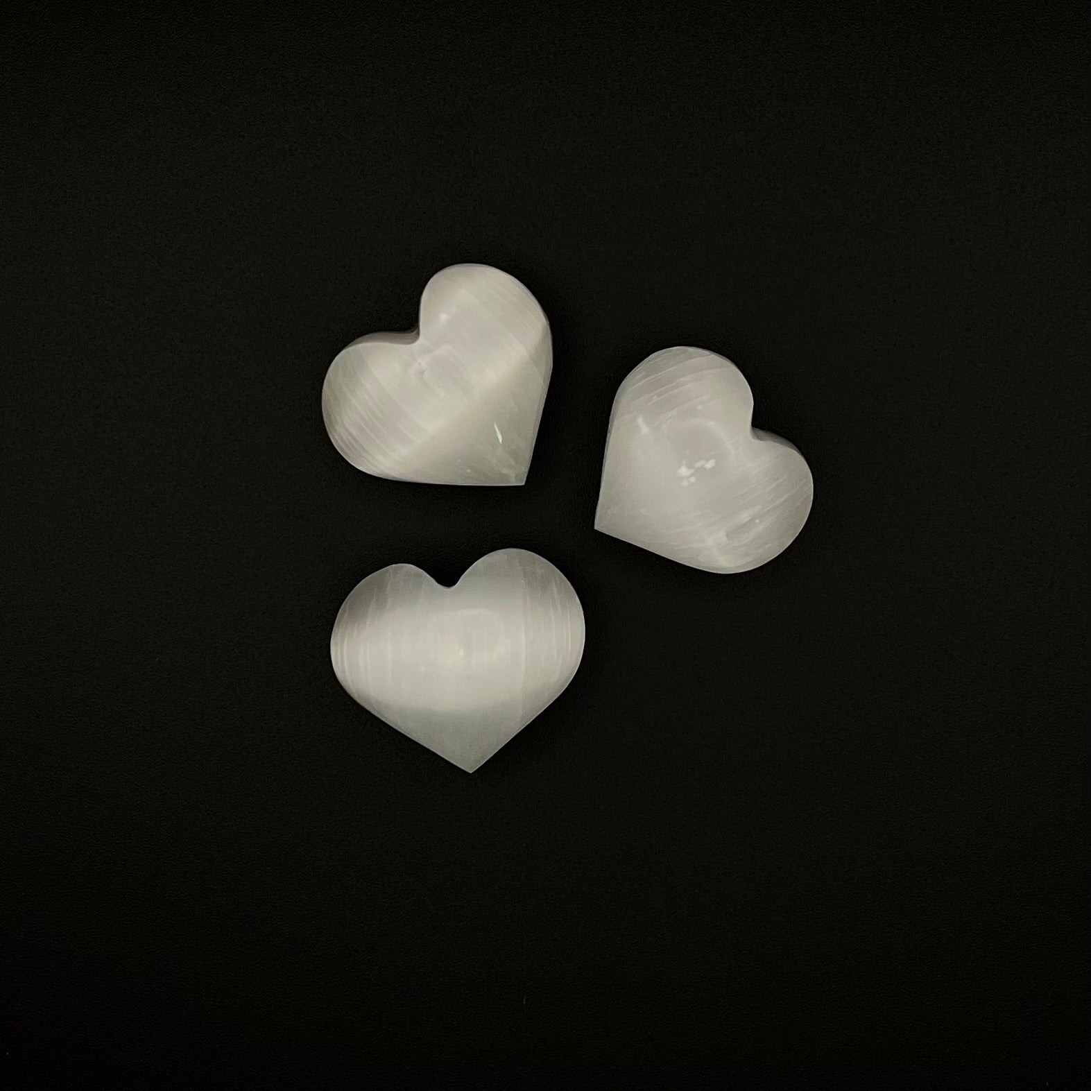 Three heart-shaped white selenite crystals arranged on a solid black background.