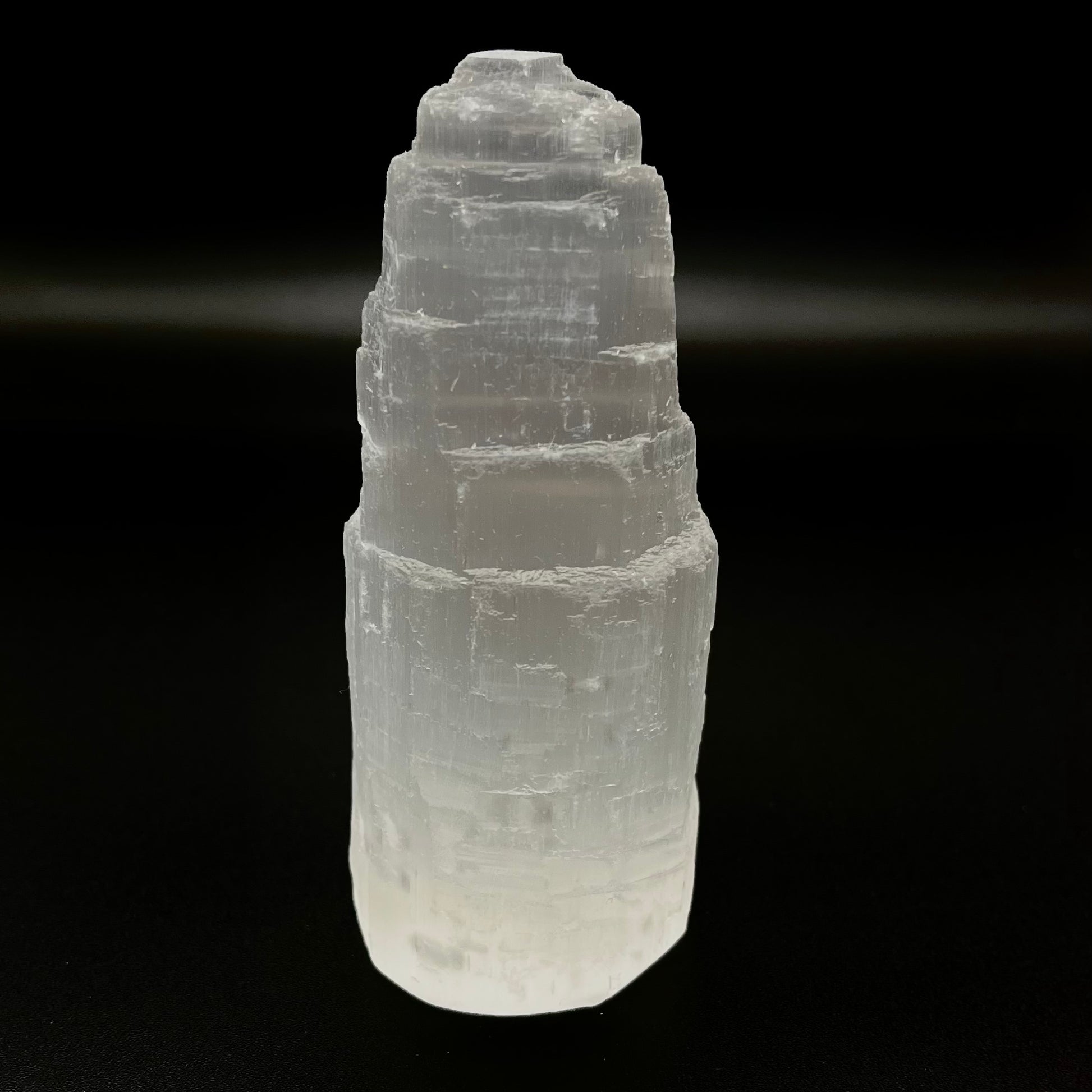 A natural white selenite tower crystal, showing layered, stacked geometric formations, photographed against a solid black background.