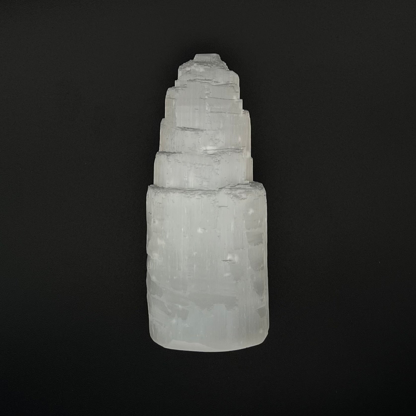 A natural white selenite tower crystal, showing layered, stacked geometric formations, photographed against a solid black background.