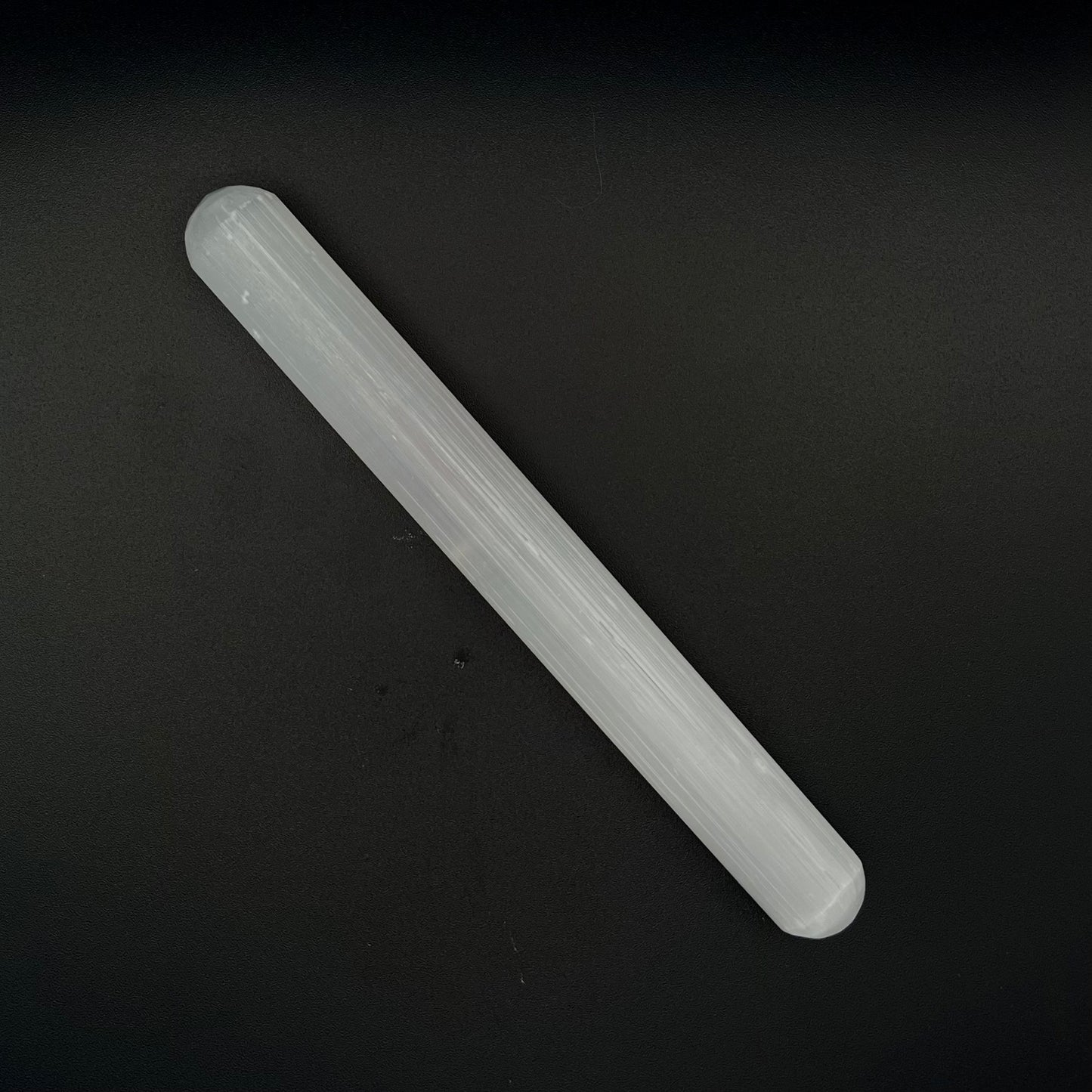 A translucent Selenite wand, placed diagonally on a dark black background.
