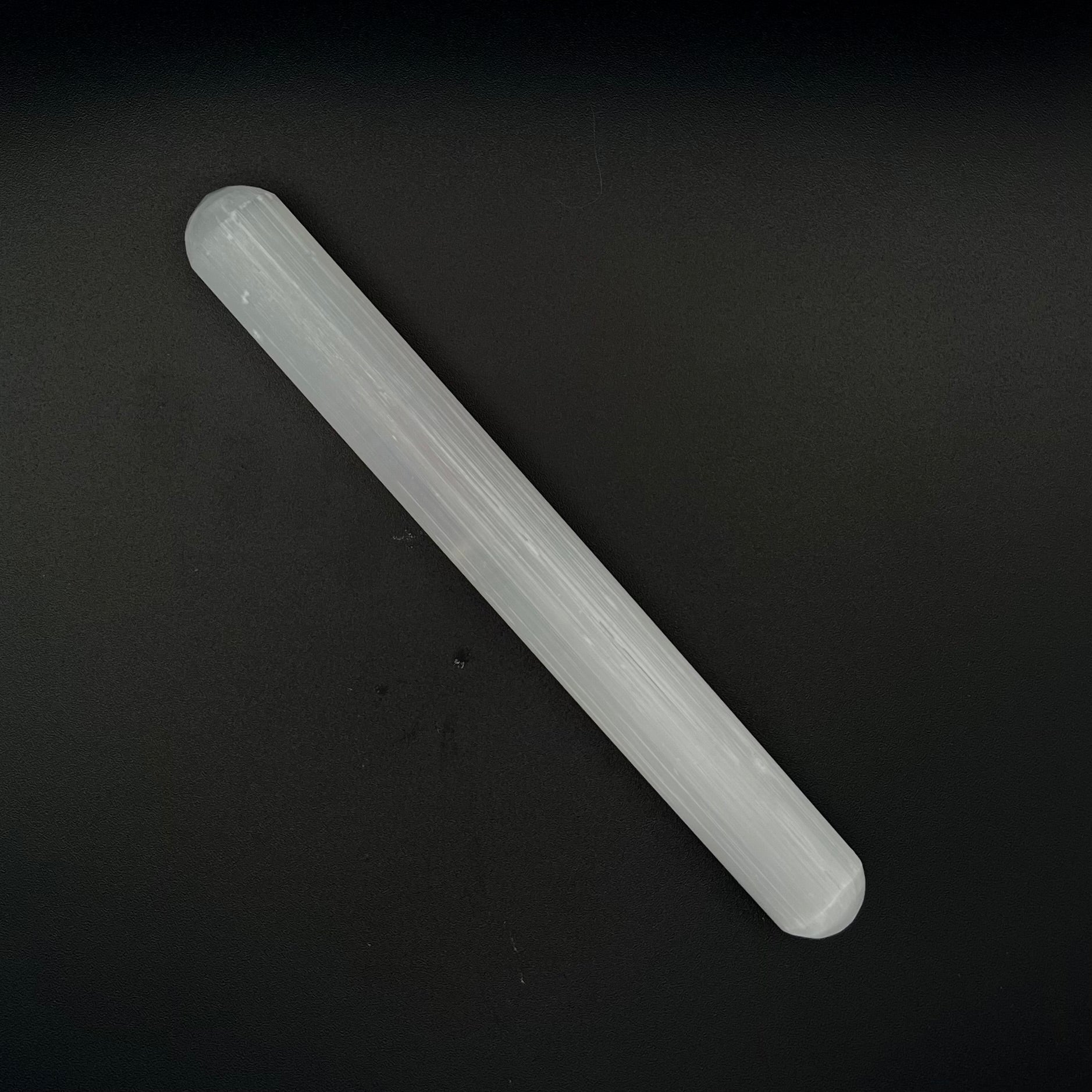 A translucent Selenite wand, placed diagonally on a dark black background.