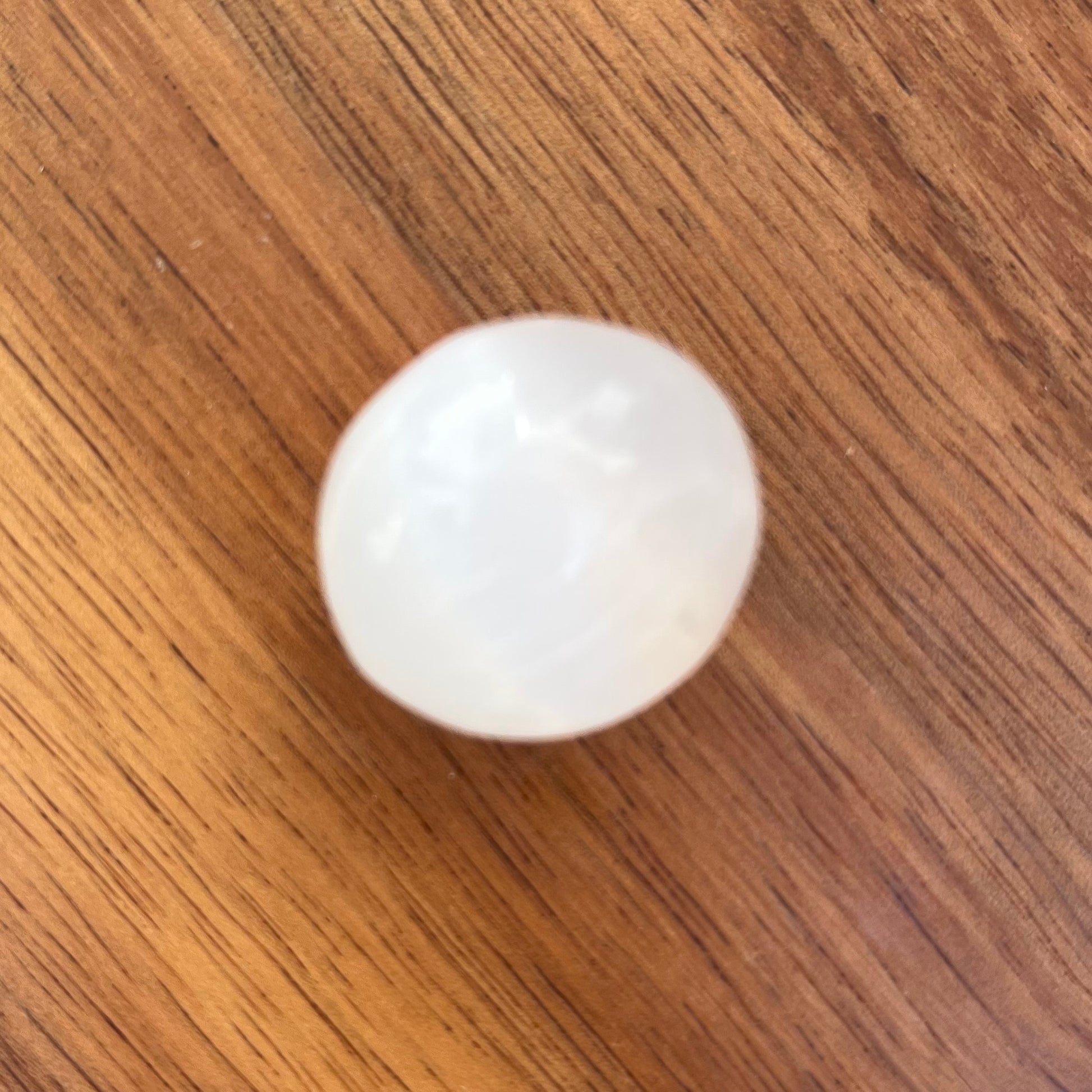 A smooth, polished white oval stone bead resting on a brown wooden surface.