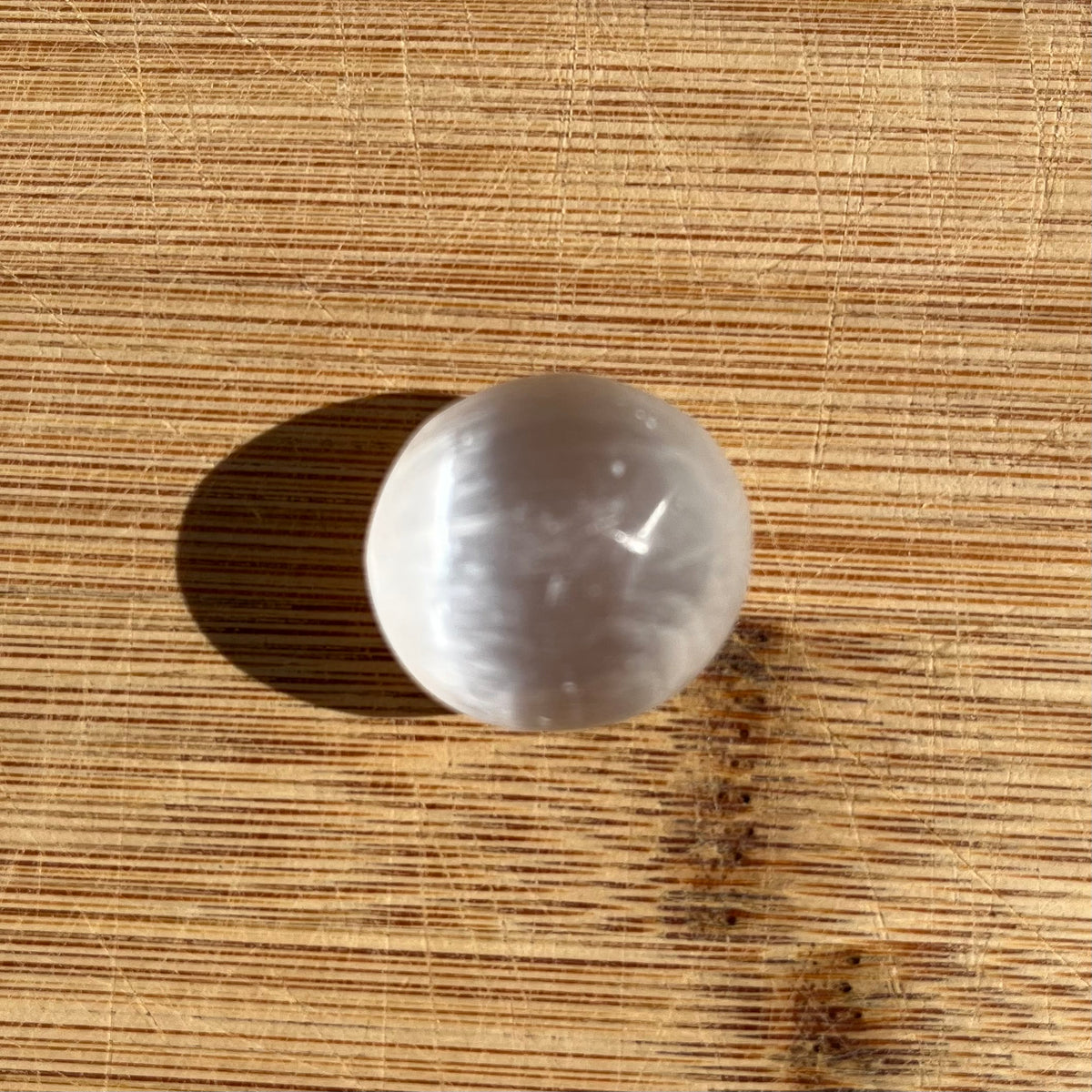 A smooth, polished white stone sphere with a milky, semi-translucent finish, resting on a textured wooden surface.