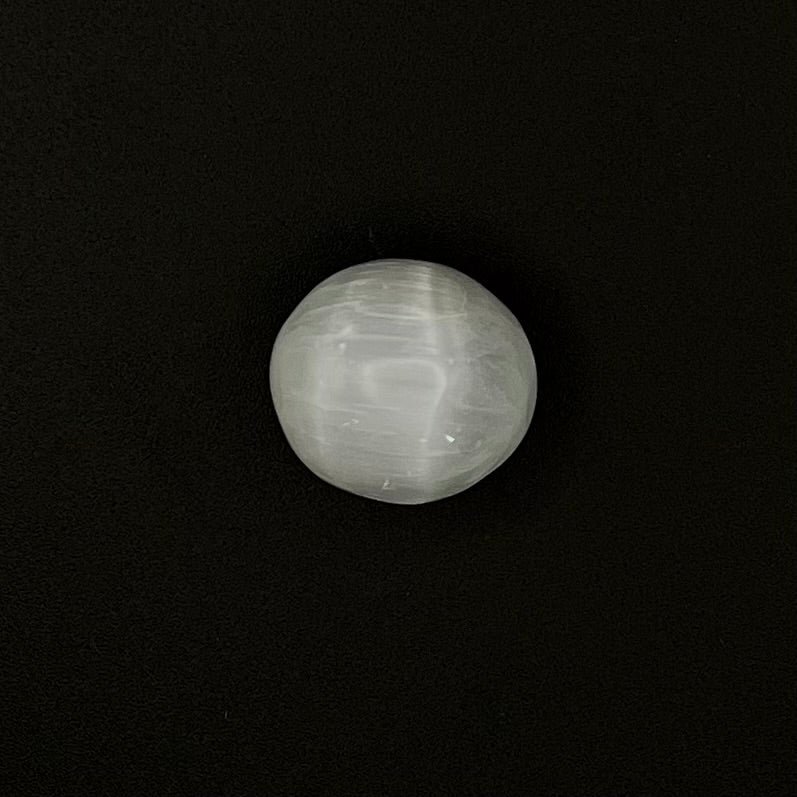 A polished white cat's eye gemstone with a strong starburst effect, shown against a solid black background.