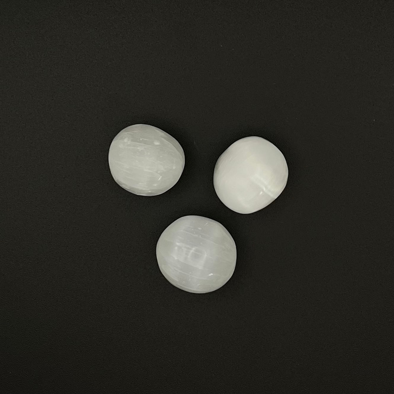 Three smooth, polished white stone beads arranged in a triangle on a dark black background.