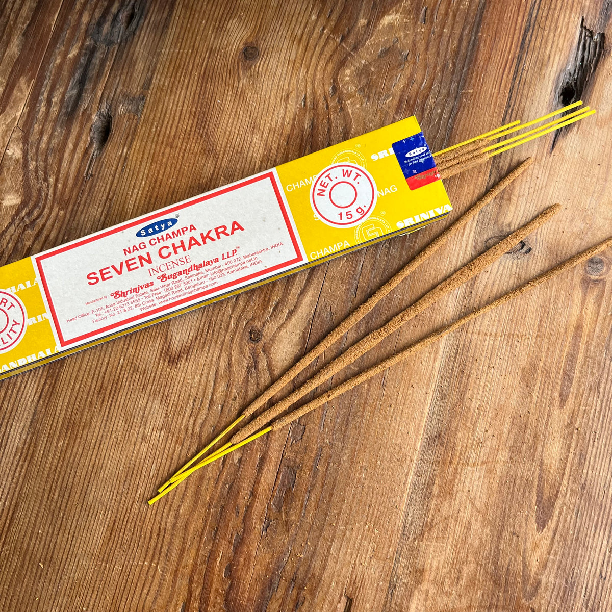 A box of Nag Champa Seven Chakra Incense sticks on a rustic wooden surface, with several brown incense sticks fanned out beside the packaging.