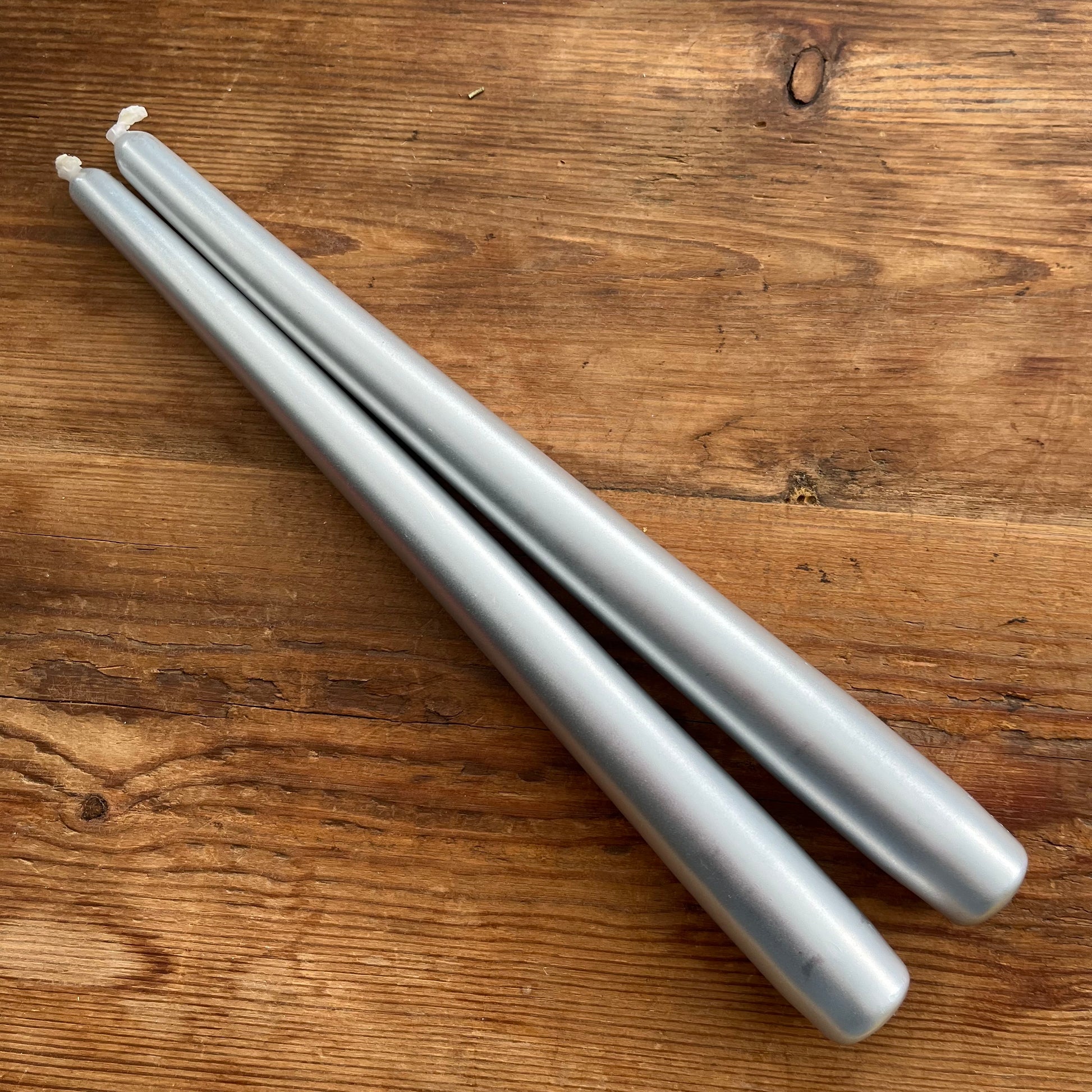 Two silver taper candles placed diagonally on a rustic wooden surface.