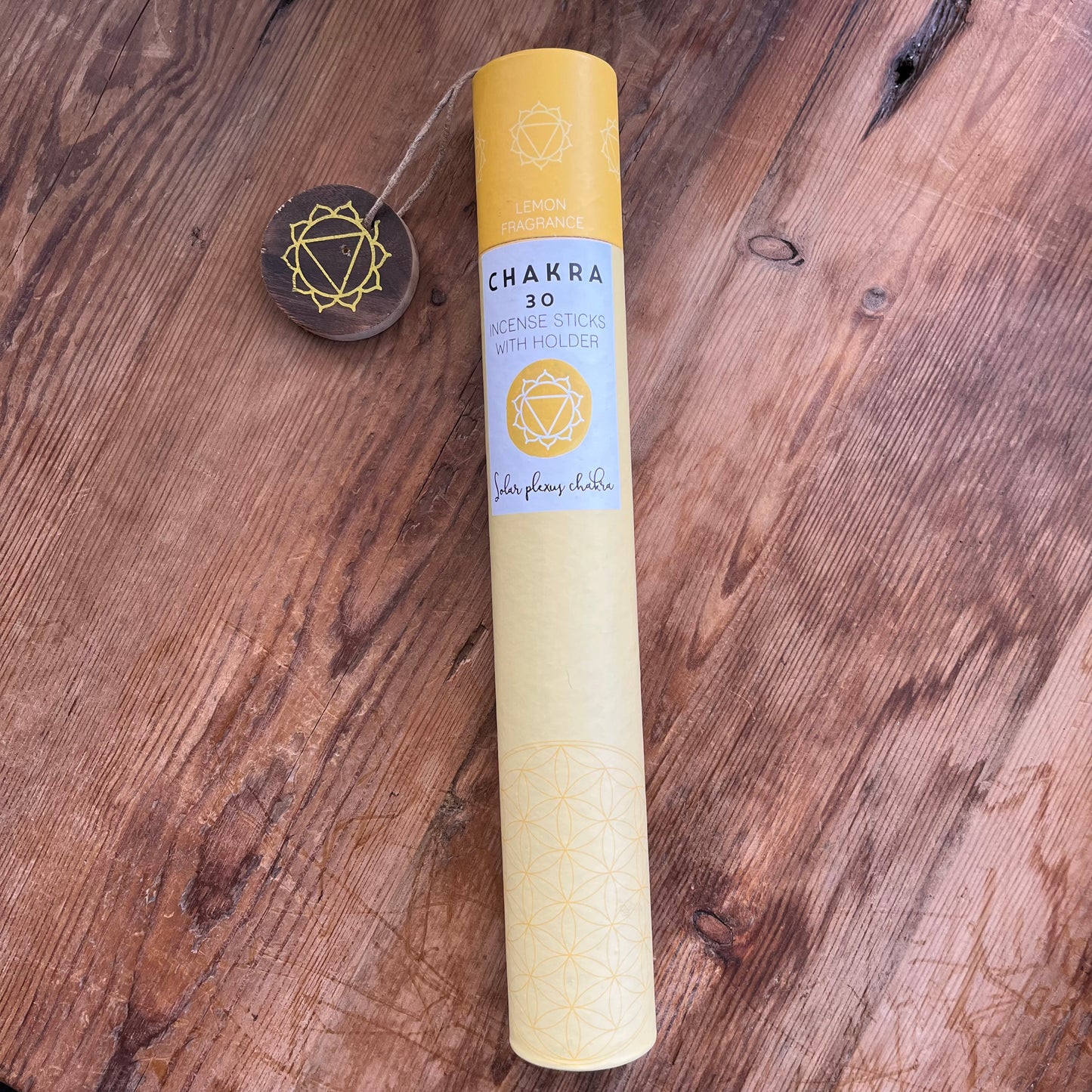 Yellow cardboard tube contining 30 sticks of lemon scented incense for the solar plexus chakra with a wooden incense holder printed withthe symbol for the solar plexus 