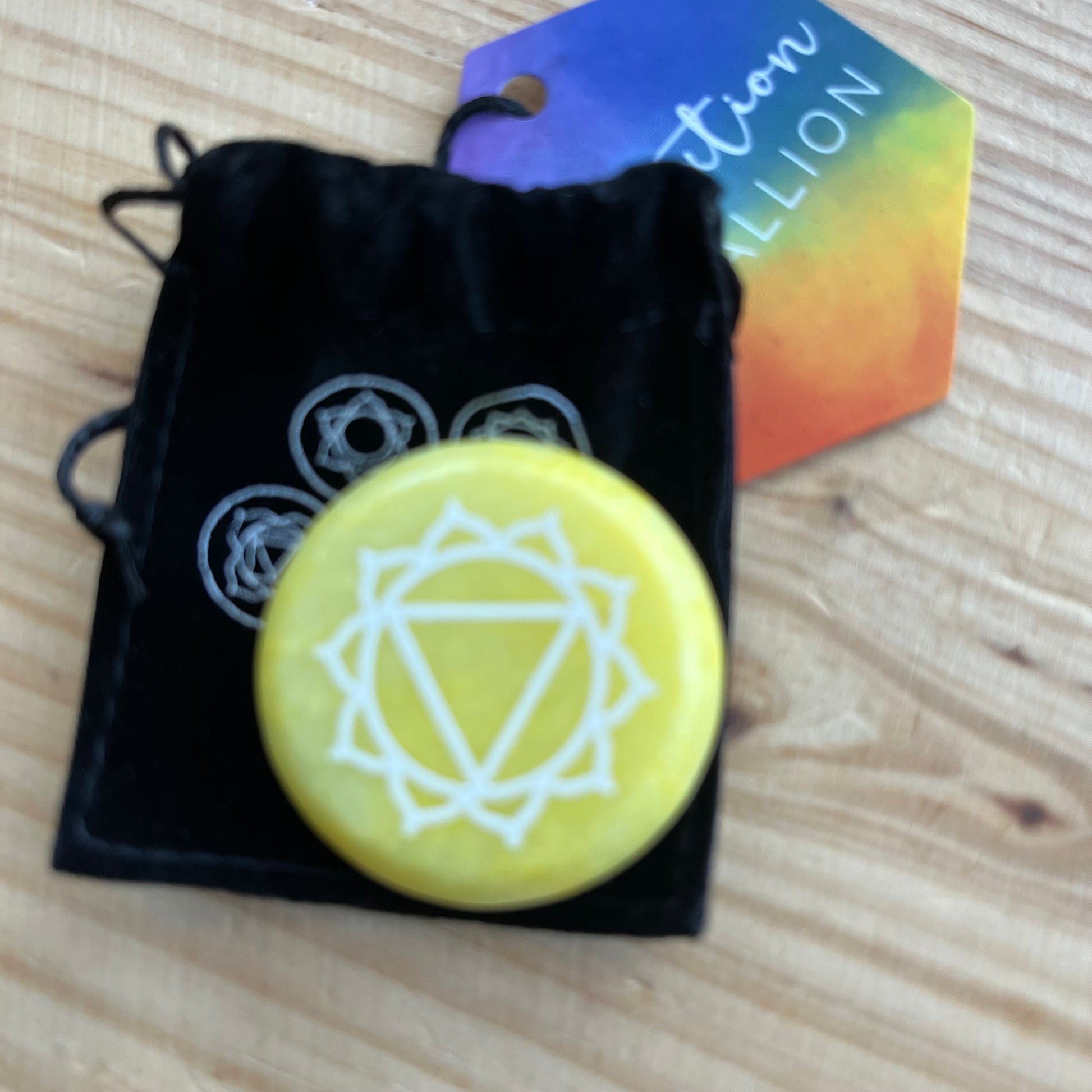 Yellow flat circular meditation stone is engraved with the Solar Plexus Chakra symbol alongside it's black velvet pouch printed with the 7 chakra symbols 