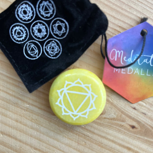 Yellow flat circular meditation stone is engraved with the Solar Plexus Chakra symbol alongside it's black velvet pouch printed with the 7 chakra symbols 