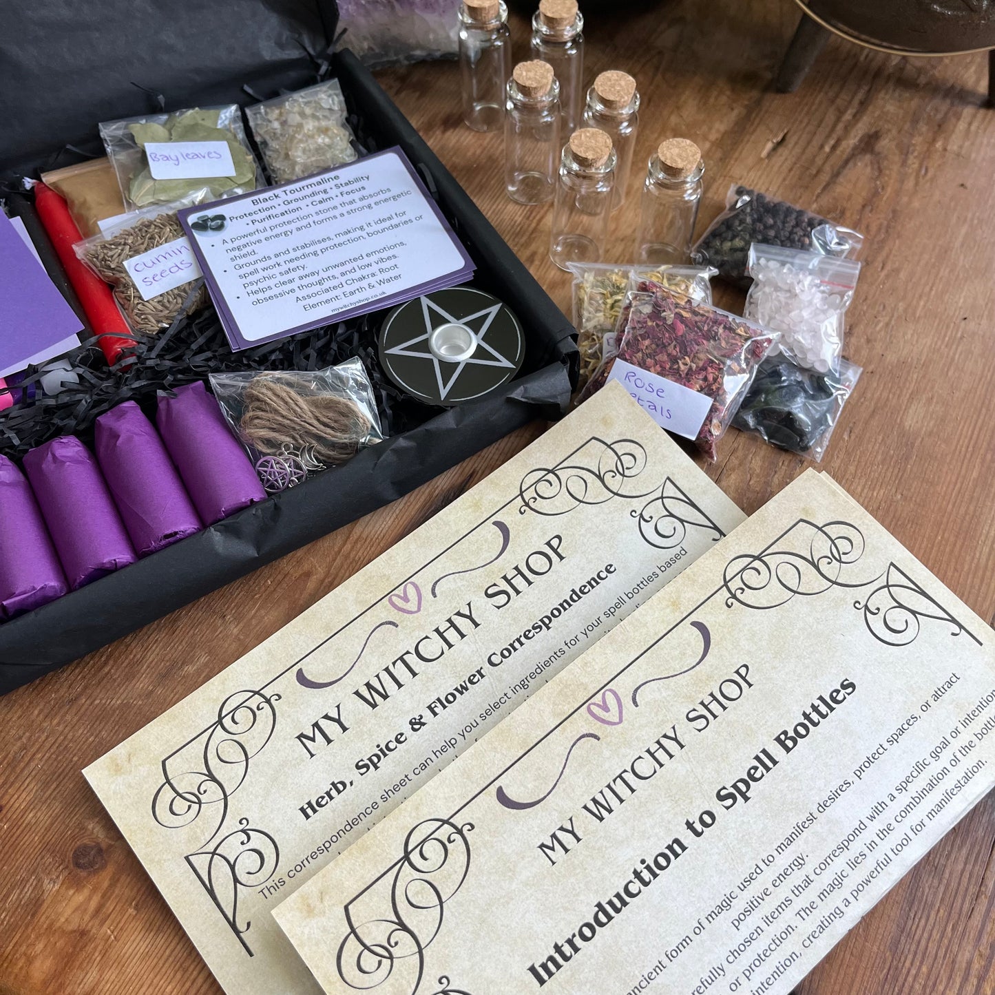 Witchcraft supplies including herbs, bottles, crystals and correspondence guide on a wooden surface with 'My Witchy Shop' branding.